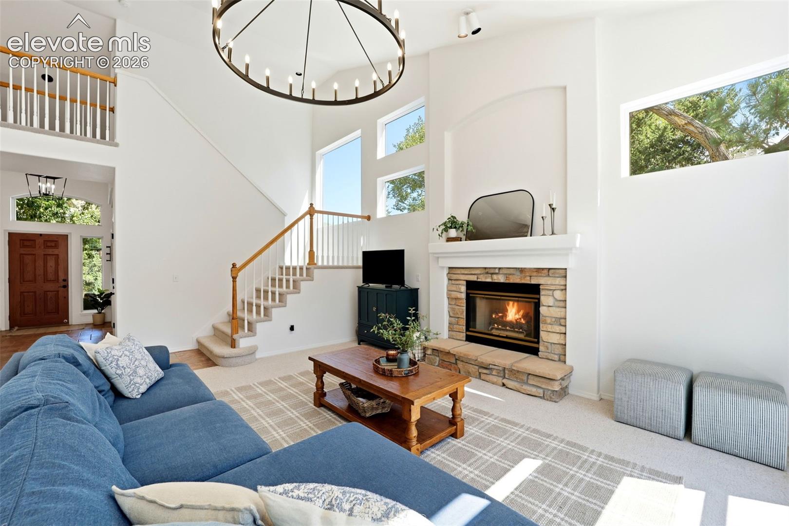 Soaring ceilings with an oversized chandelier, stone-surround fireplace, large windows