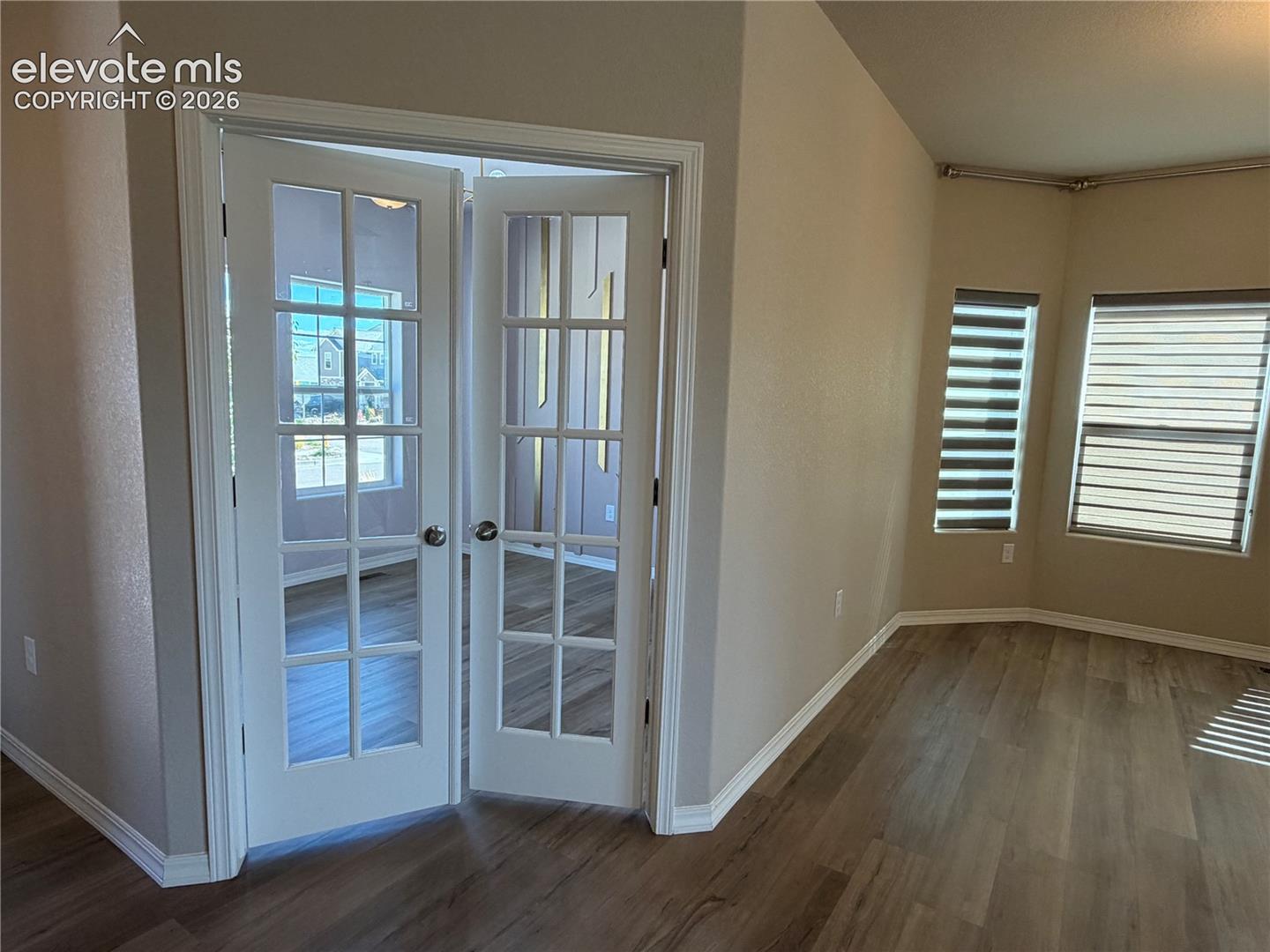 French doors with multiple lites, wood-finish flooring, two windows with horizontal blinds, and neutral wall tones