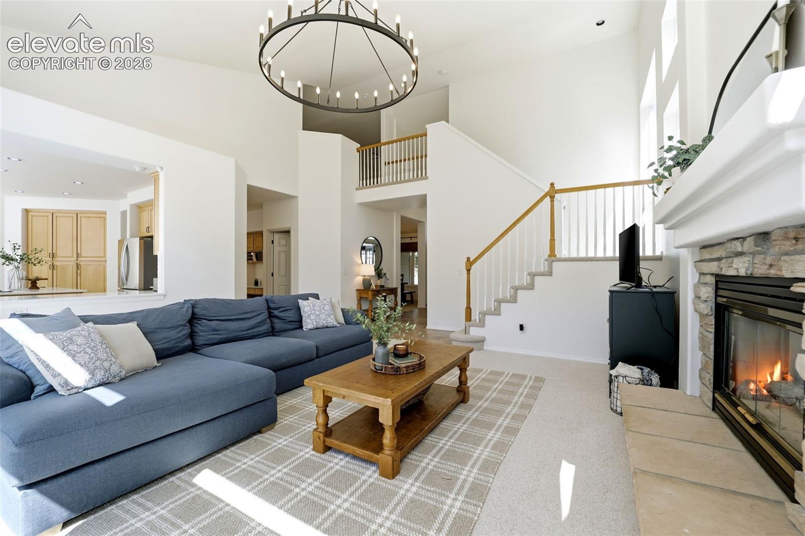 Two-story living area with a stone-clad fireplace and white mantel, a grand staircase with wood railing, and a second-level balcony