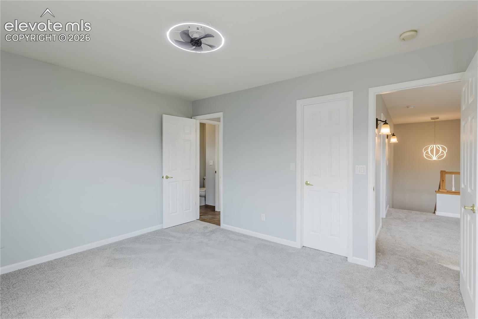Light gray wall finish, gray carpet flooring, contemporary ceiling fan, white paneled doors, and brushed gold hardware