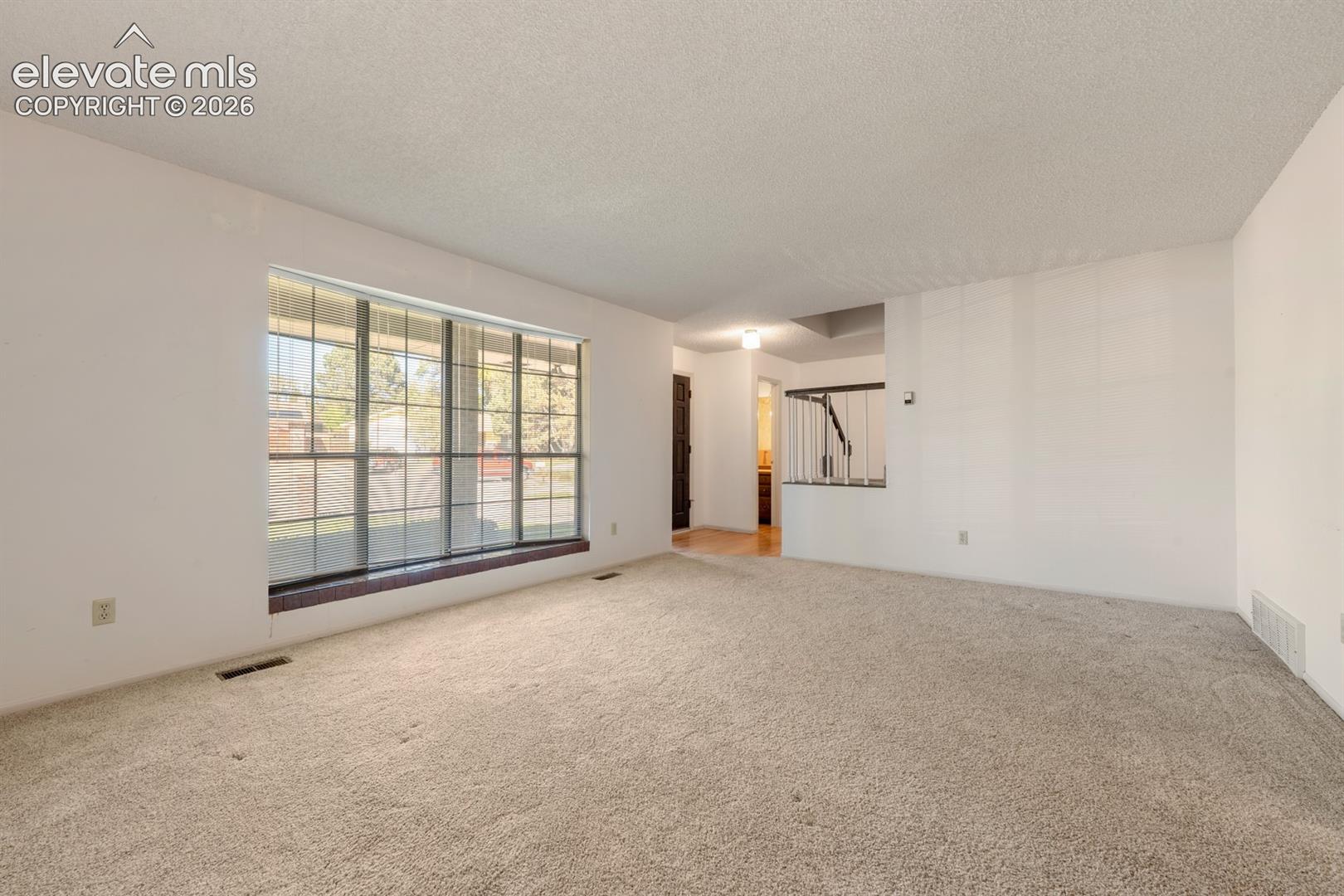Living area featuring a large picture window, brick-surround window seat, wall-to-wall carpeting, and a built-in metal railing