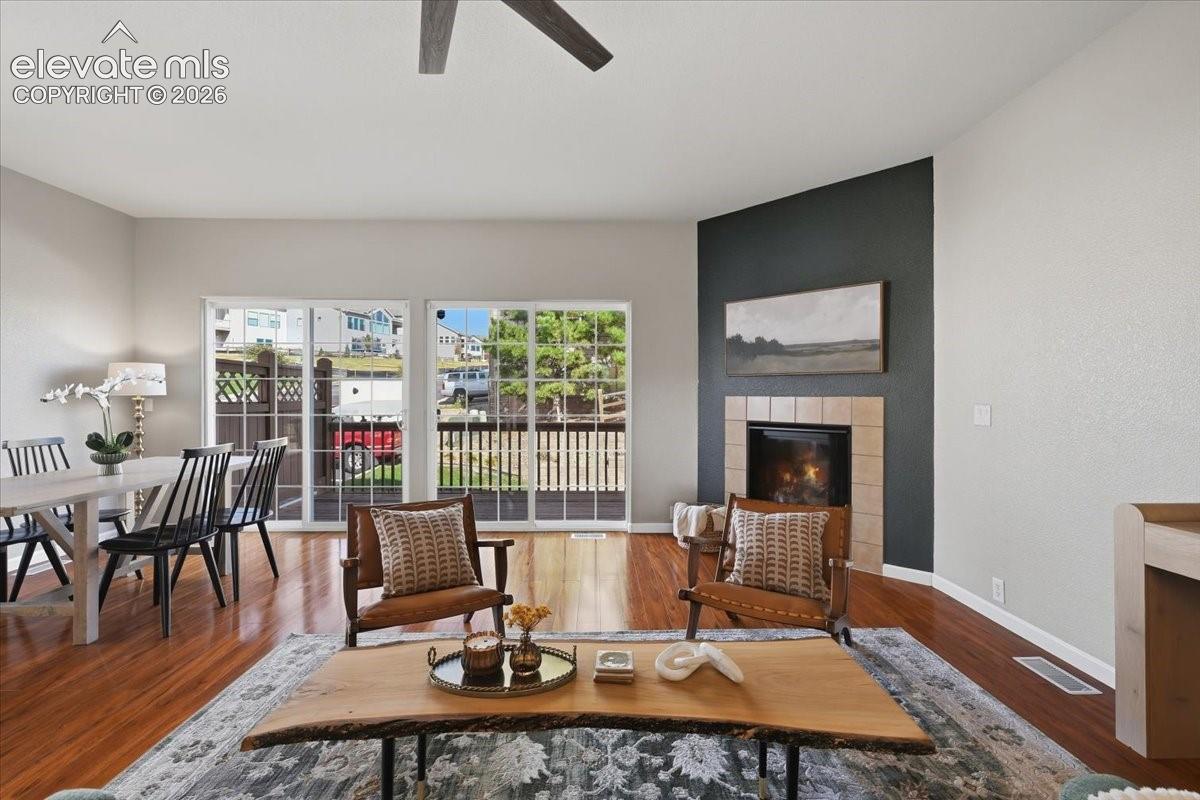 Hardwood flooring, tiled fireplace surround, high ceilings, ceiling fan, and sliding glass doors