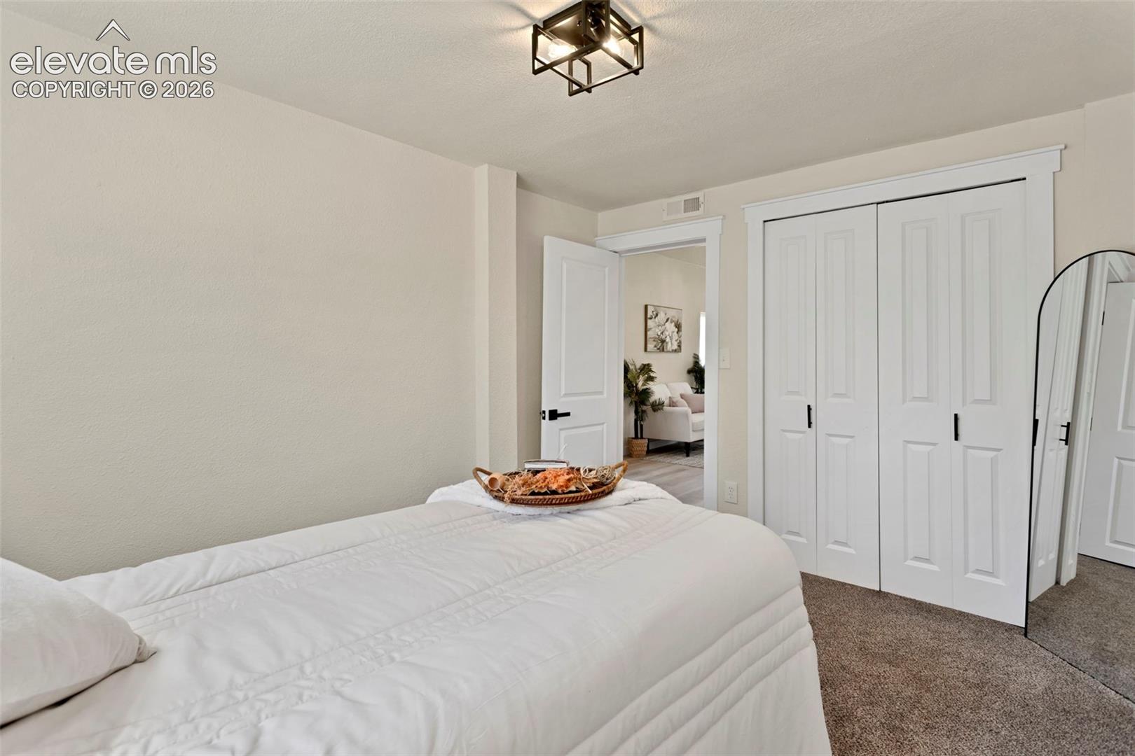 Bedroom featuring neutral wall paint, carpet flooring, a white bi-fold closet, and a contemporary ceiling light fixture