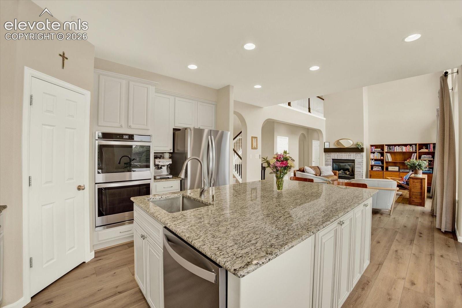 Kitchen featuring a large central island with a stone countertop and undermount sink, white cabinetry, stainless steel double wall ovens, and wood-finish flooring