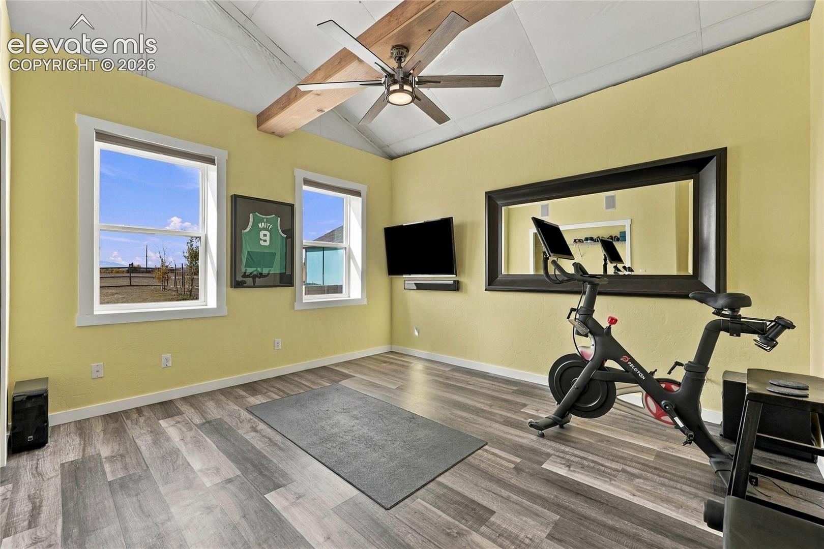 Vaulted ceiling with an exposed wood beam, wood-finish flooring, and a ceiling fan with integrated lighting