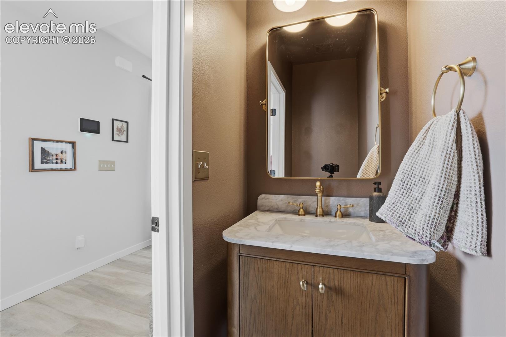 Bathroom vanity featuring a light-toned countertop, brass-finish faucet, and coordinating framed mirror