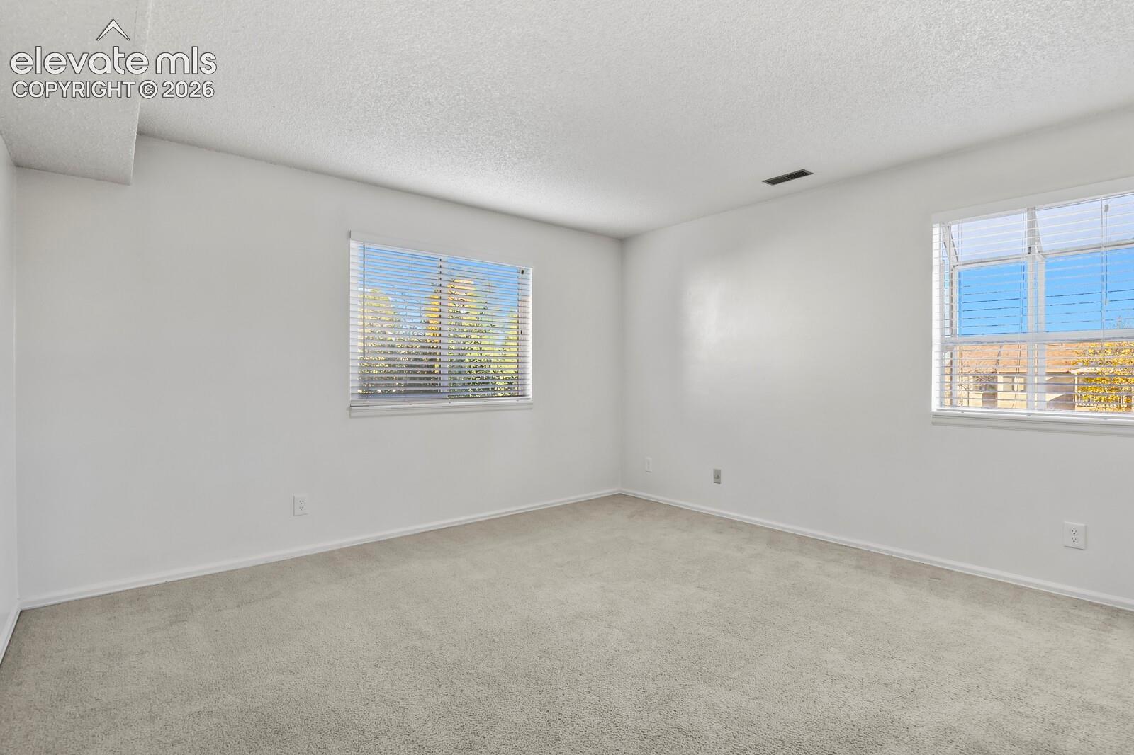 Neutral-toned interior space featuring light-colored wall-to-wall carpeting, white walls, and two windows with blinds