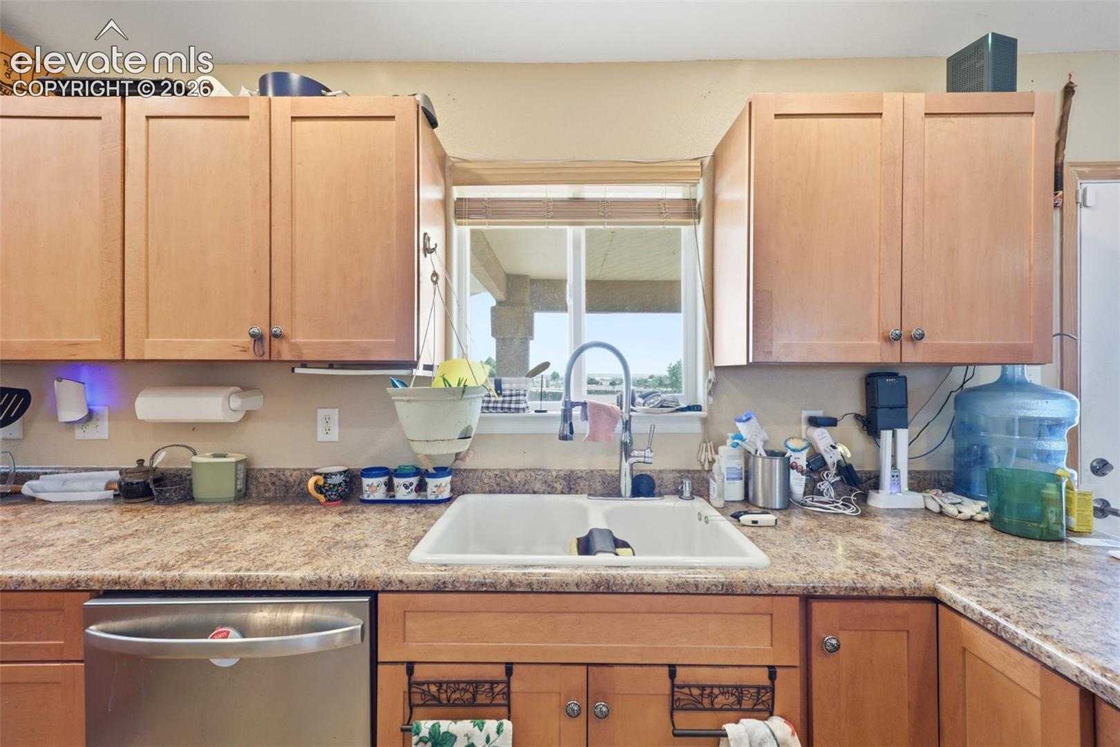 Kitchen featuring light wood cabinetry, a double basin sink with a high-arch faucet, a stainless steel dishwasher, and mottled laminate countertops