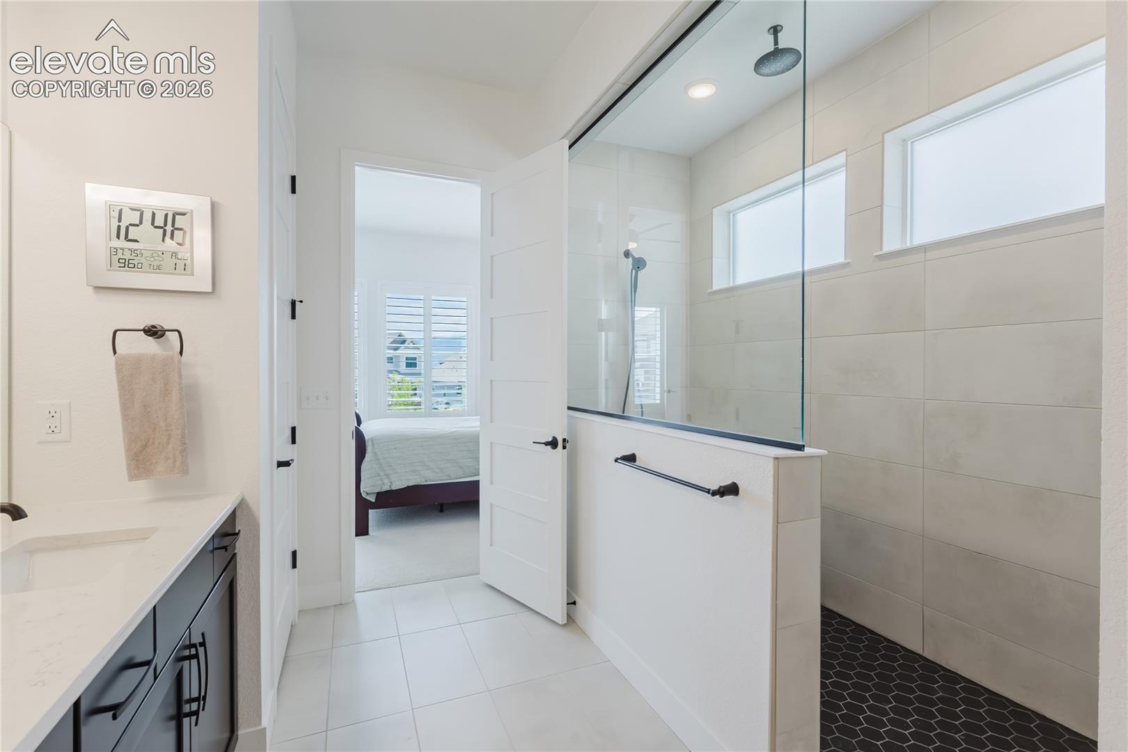 Walk-in shower with clear glass enclosure, rainfall showerhead and  a second showerhead, and black hexagonal tile flooring