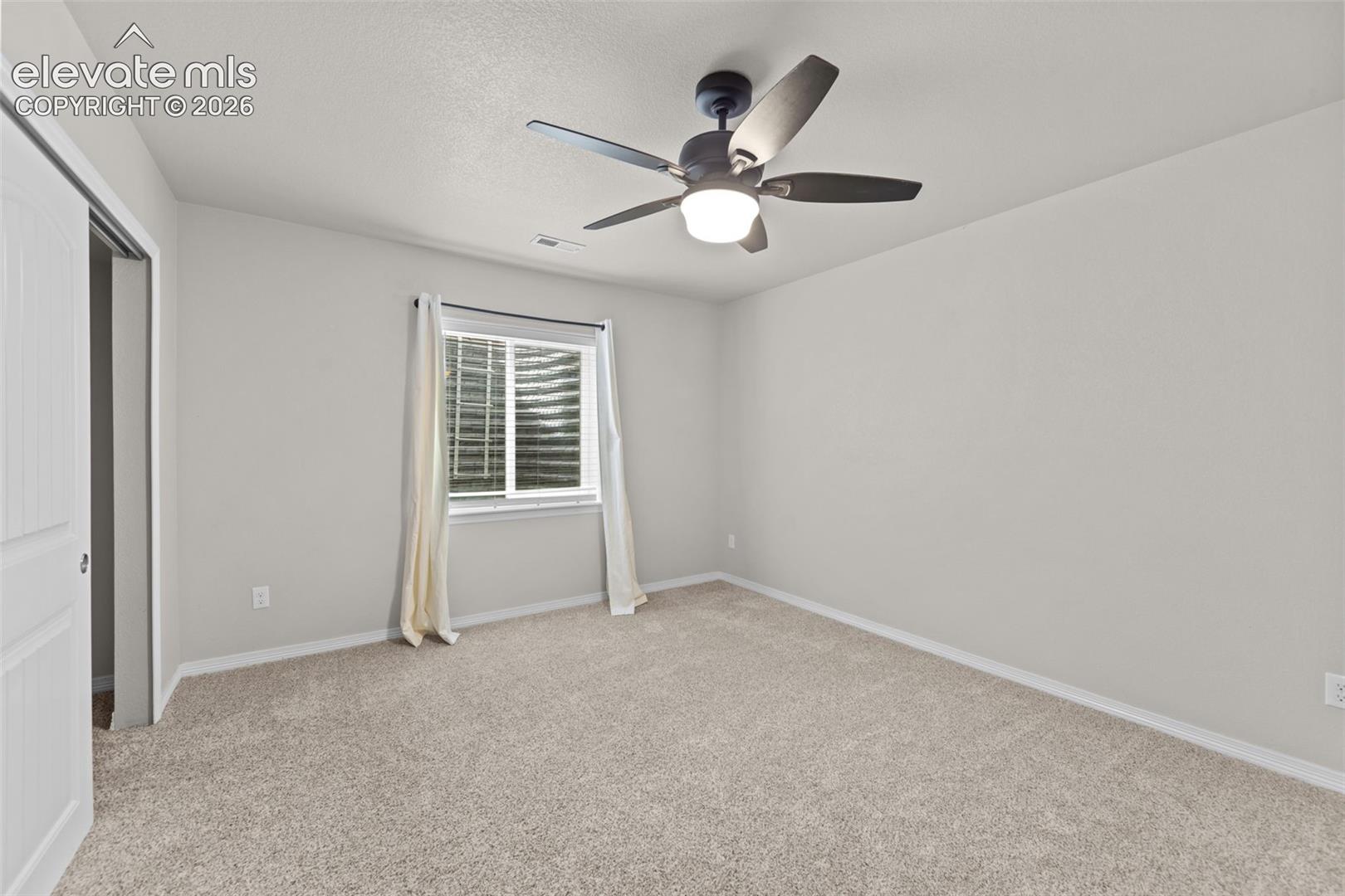 Wall-to-wall carpeting with light-toned walls, featuring a window and a ceiling fan with integrated lighting