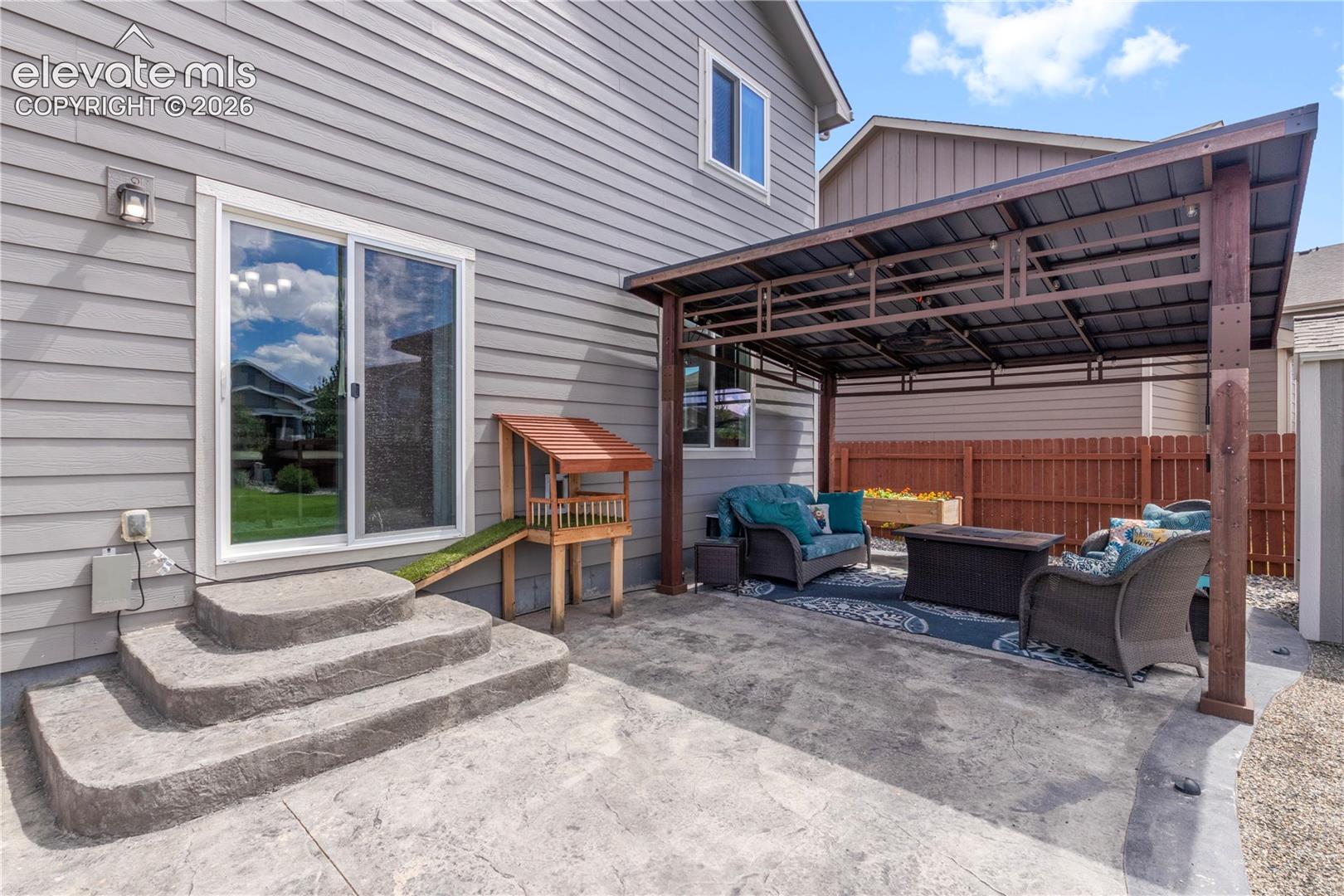 Expansive stamped concrete patio featuring a covered pergola, sliding glass door access, and exterior wall siding