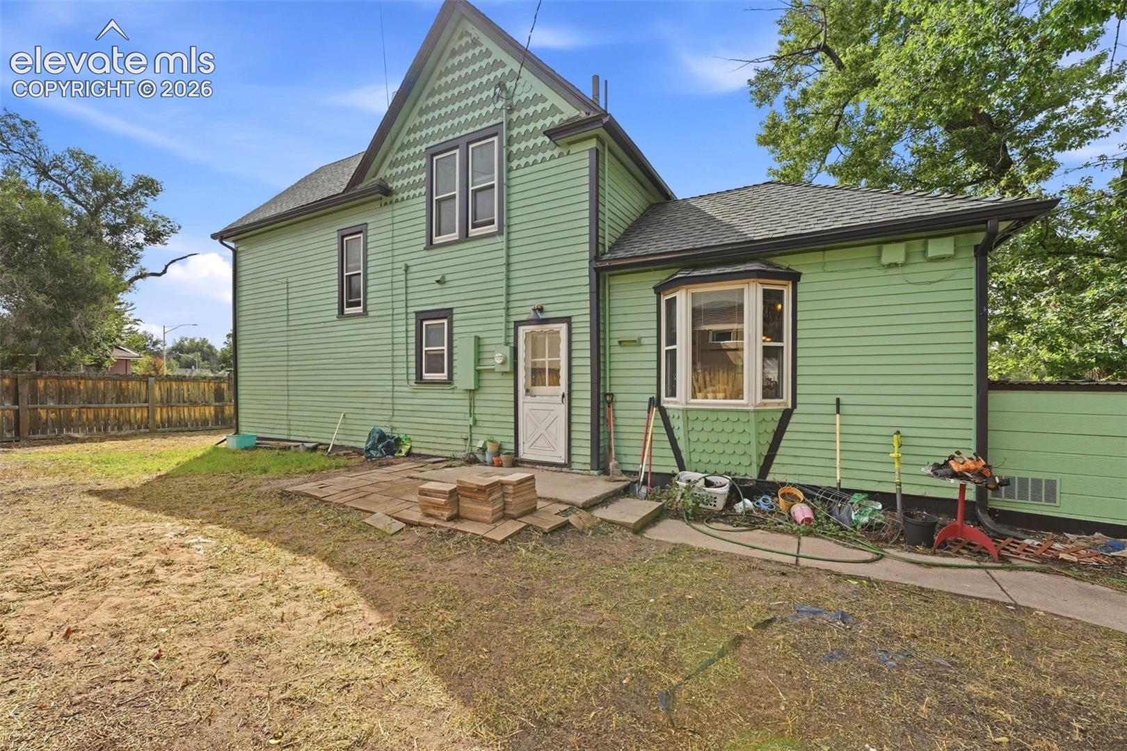Rear exterior showcasing light green siding, black trim, a bay window, and a gabled roof