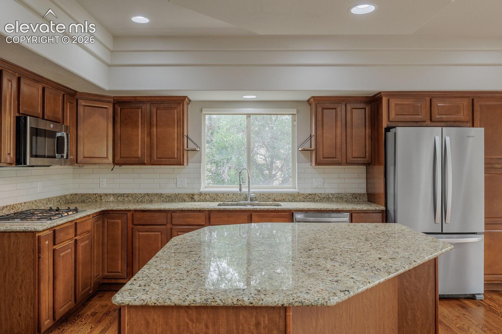 Chef's kitchen featuring warm wood cabinetry, speckled granite countertops, and a substantial center island with seating