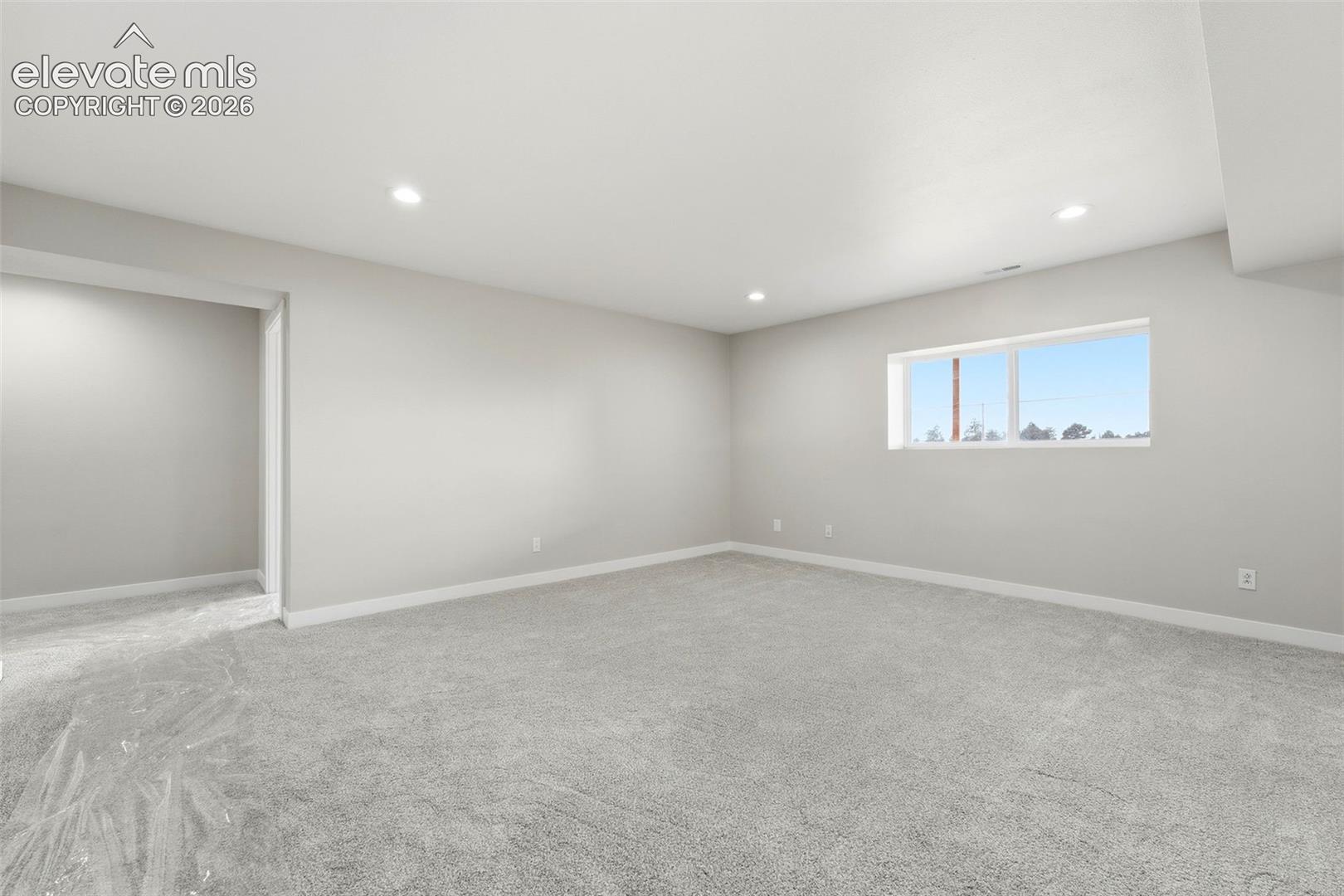 Recessed lighting illuminates the neutral-toned walls and soft gray carpeting