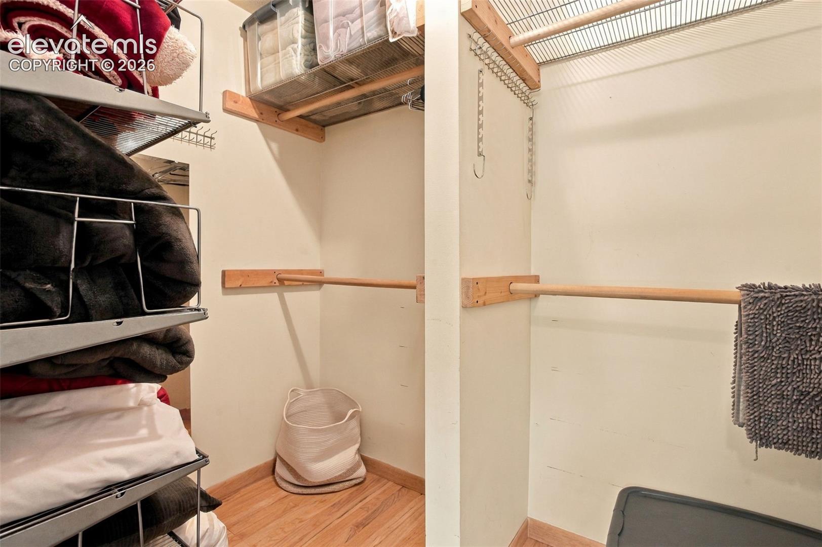 Walk-in storage space featuring wood-finish flooring, mounted wooden hanging rods, and integrated wire shelving units