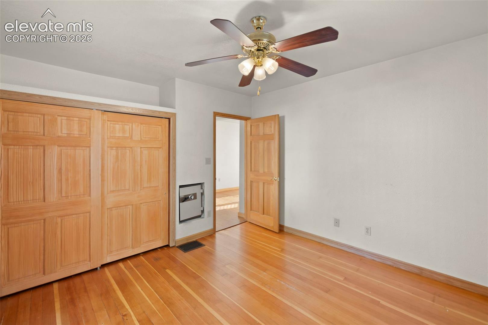 Wood-finish flooring with baseboard trim, sliding paneled closet doors, and a ceiling fan with light fixture