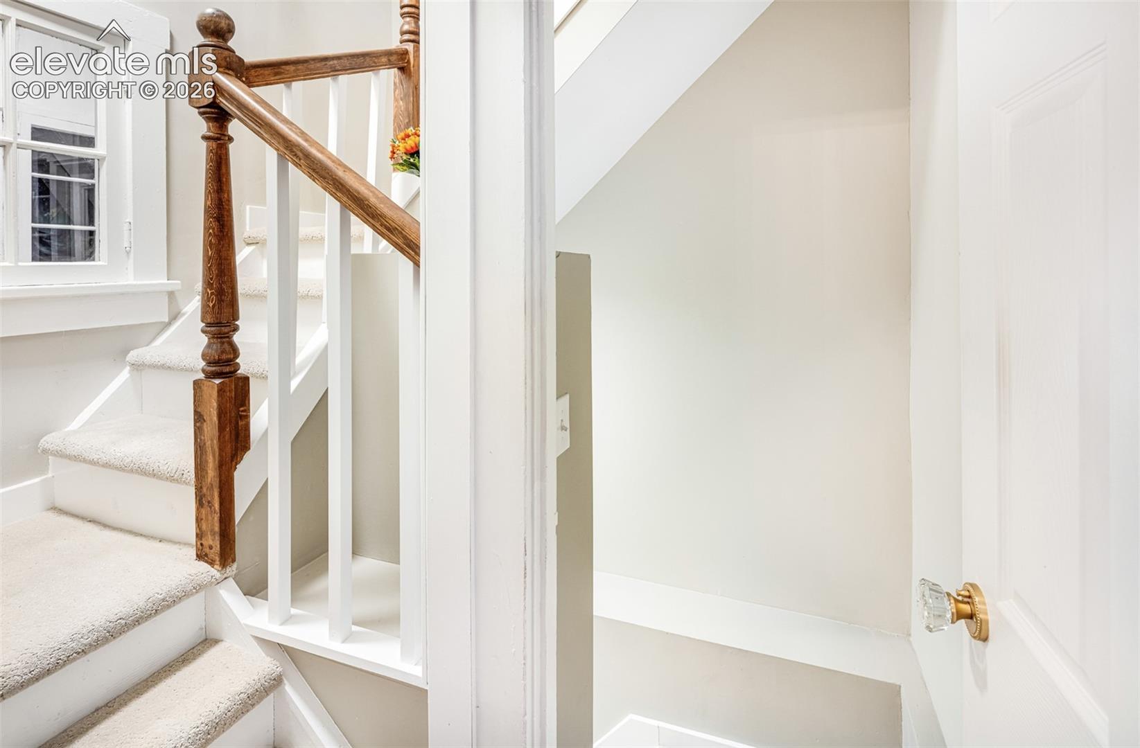 Carpeted staircase with a wood handrail and white balusters
