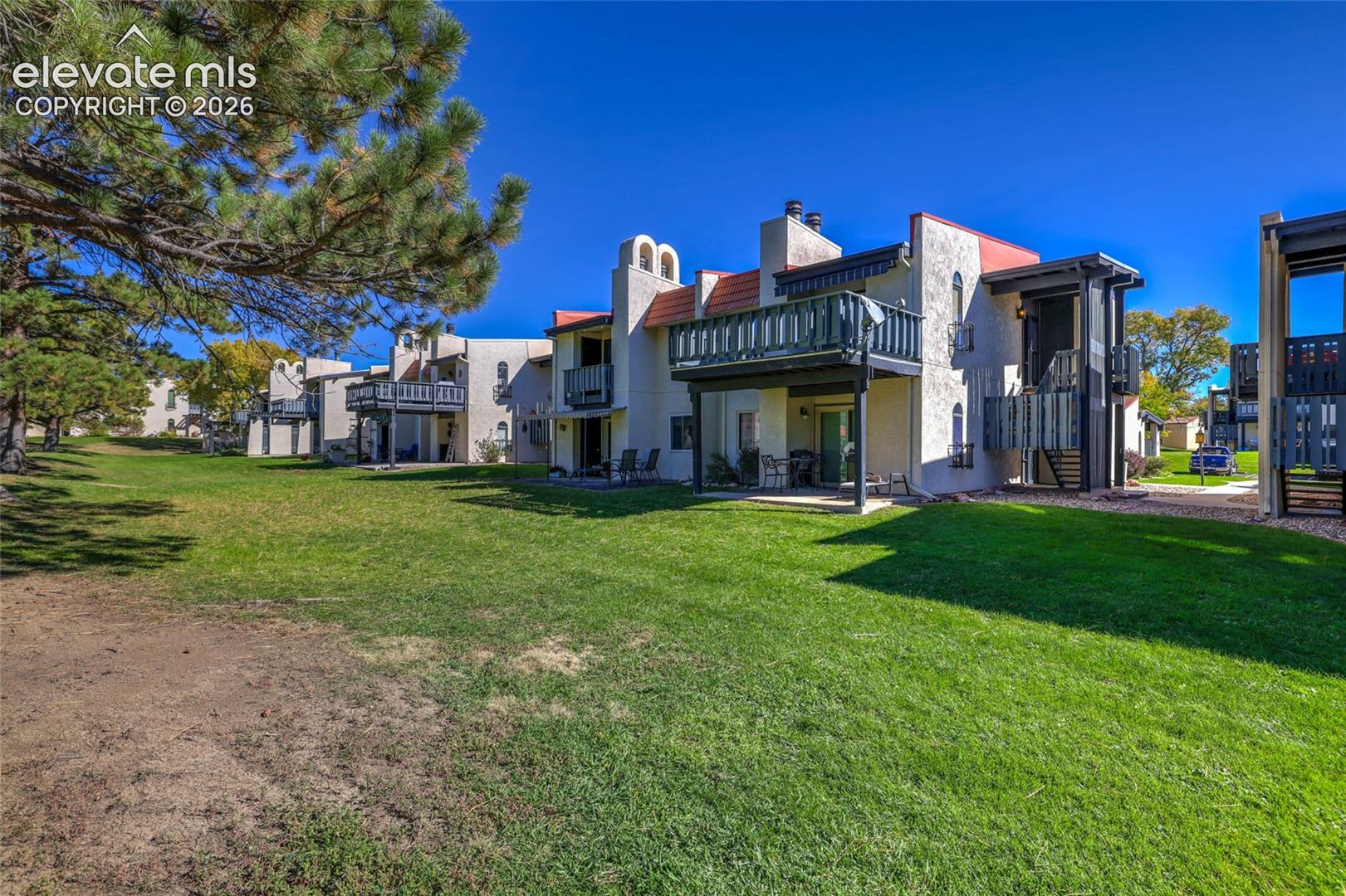Exterior featuring multi-level stucco architecture, metal balconies, tile roof accents, and expansive common green space