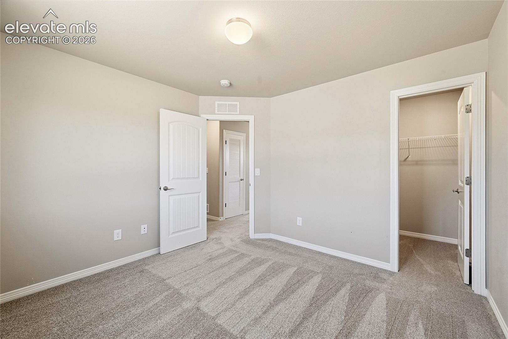 Neutral-toned interior room featuring light gray walls, plush patterned carpeting, and white baseboards