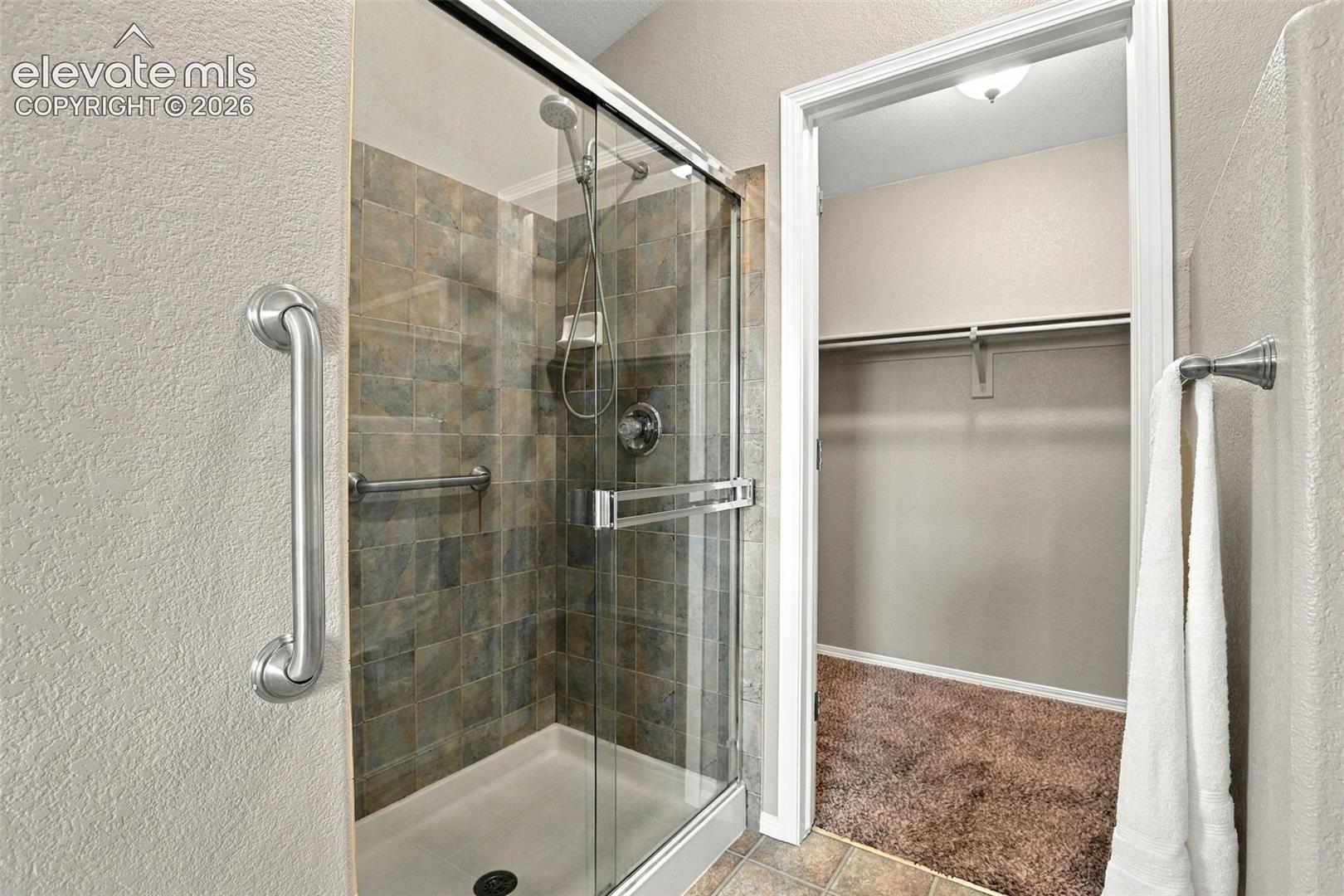 Glass-enclosed shower with tiled surround, handheld shower fixture, and built-in grab bars