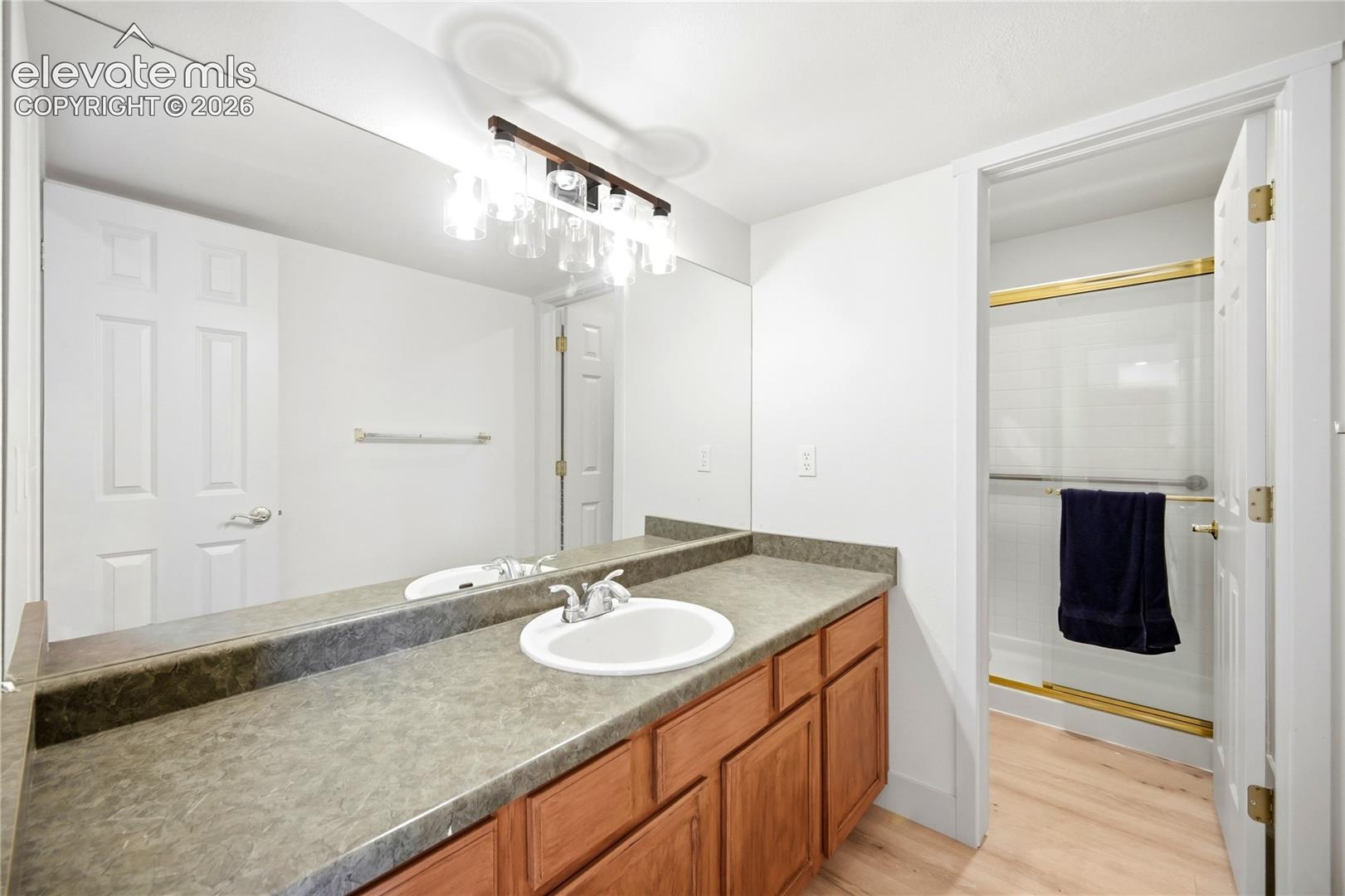 Wood-finish vanity cabinet, solid-surface countertop with integrated oval sink, full-width wall mirror, multi-light fixture, and light-toned wood-finish flooring