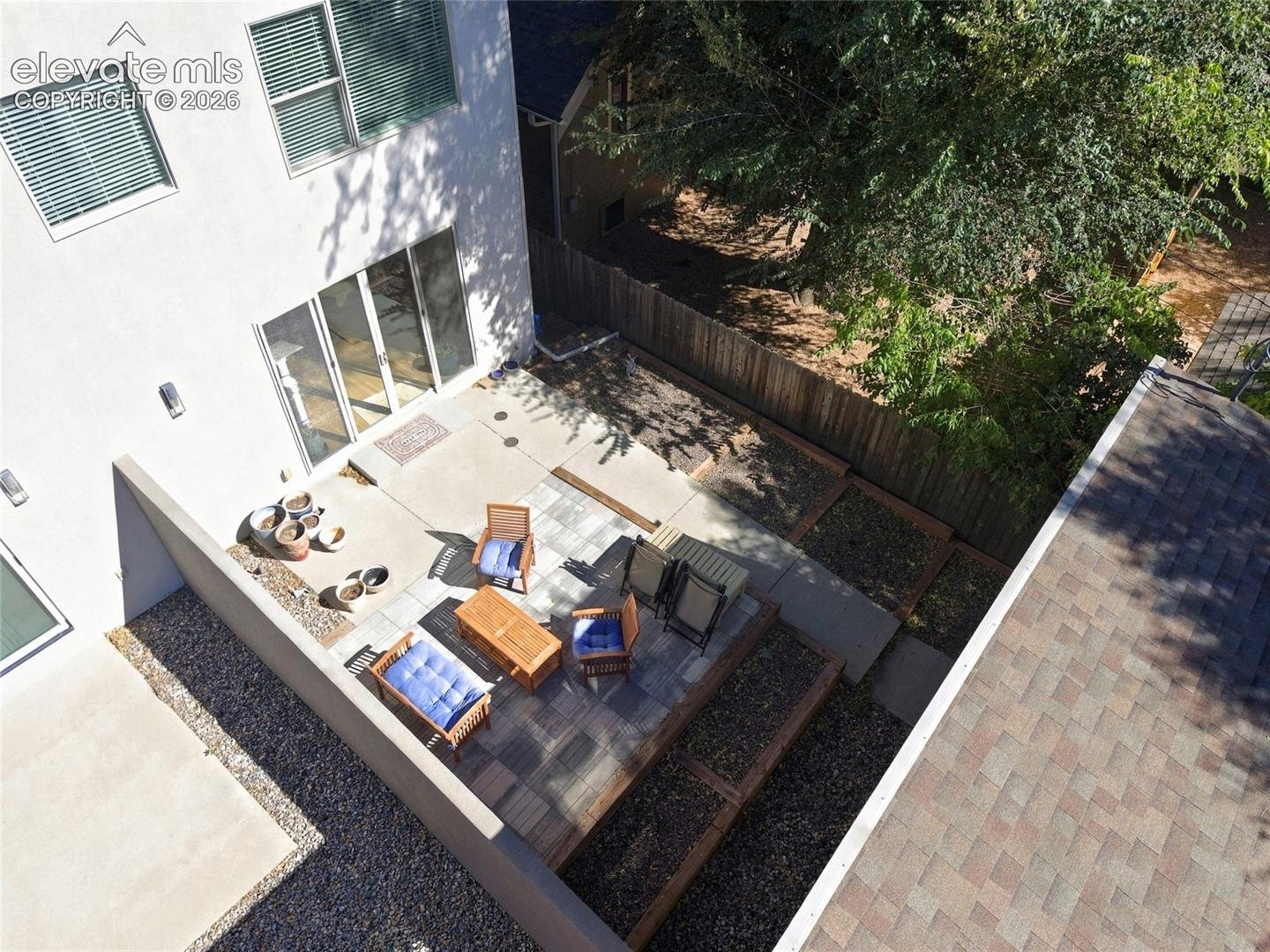 Exterior courtyard featuring a concrete patio, tiered wooden retaining walls, gravel landscaping, and a fenced perimeter