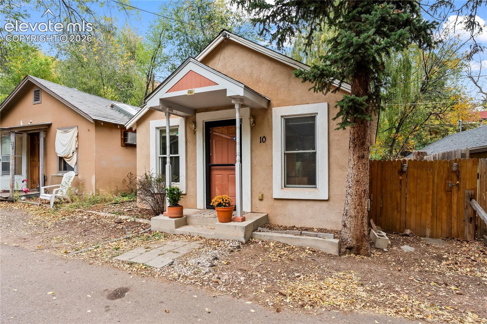 Stucco exterior featuring a covered front porch with decorative posts, concrete entry steps, and wood-panel fencing