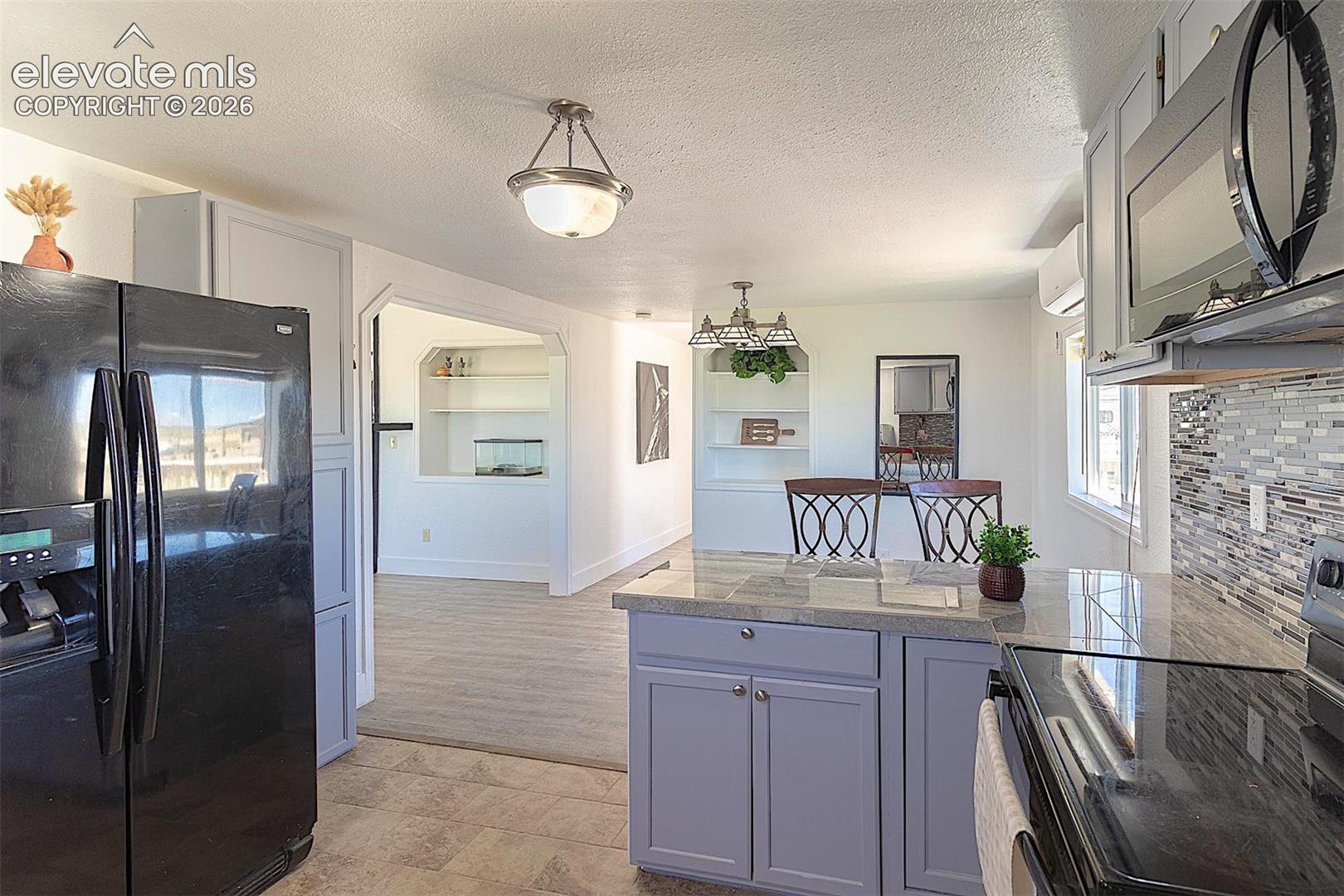 Kitchen featuring black appliances, tile counters, a peninsula, built in features, and a textured ceiling