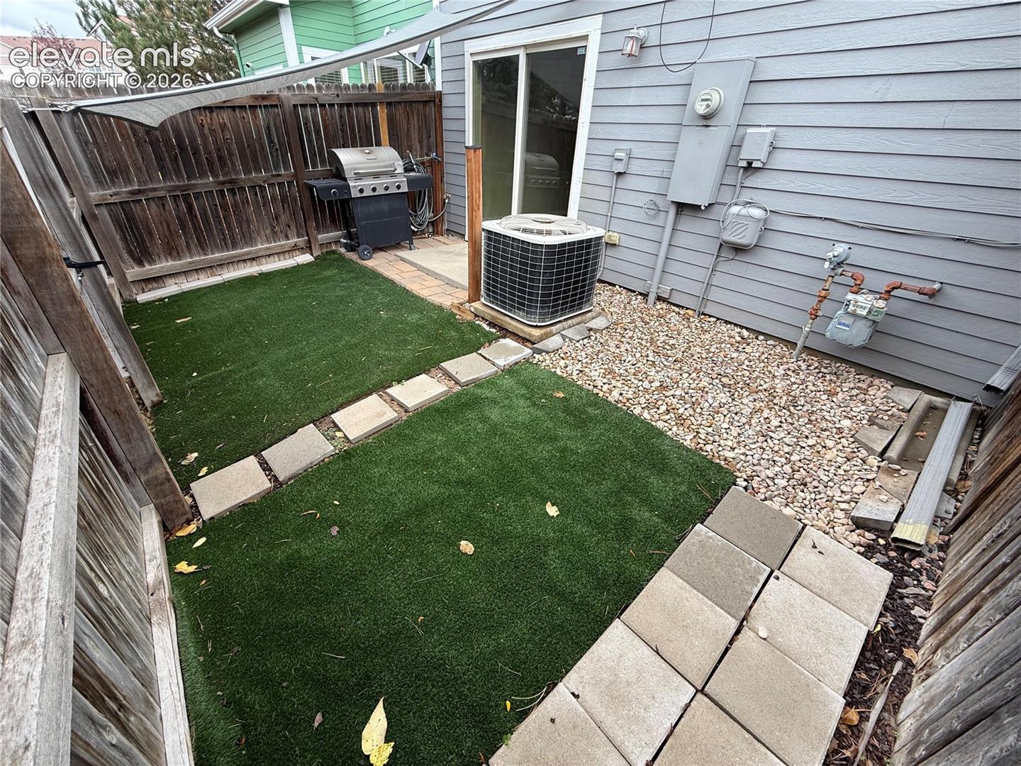 Fenced back featuring artificial turf, stone paver pathway, gravel ground cover
