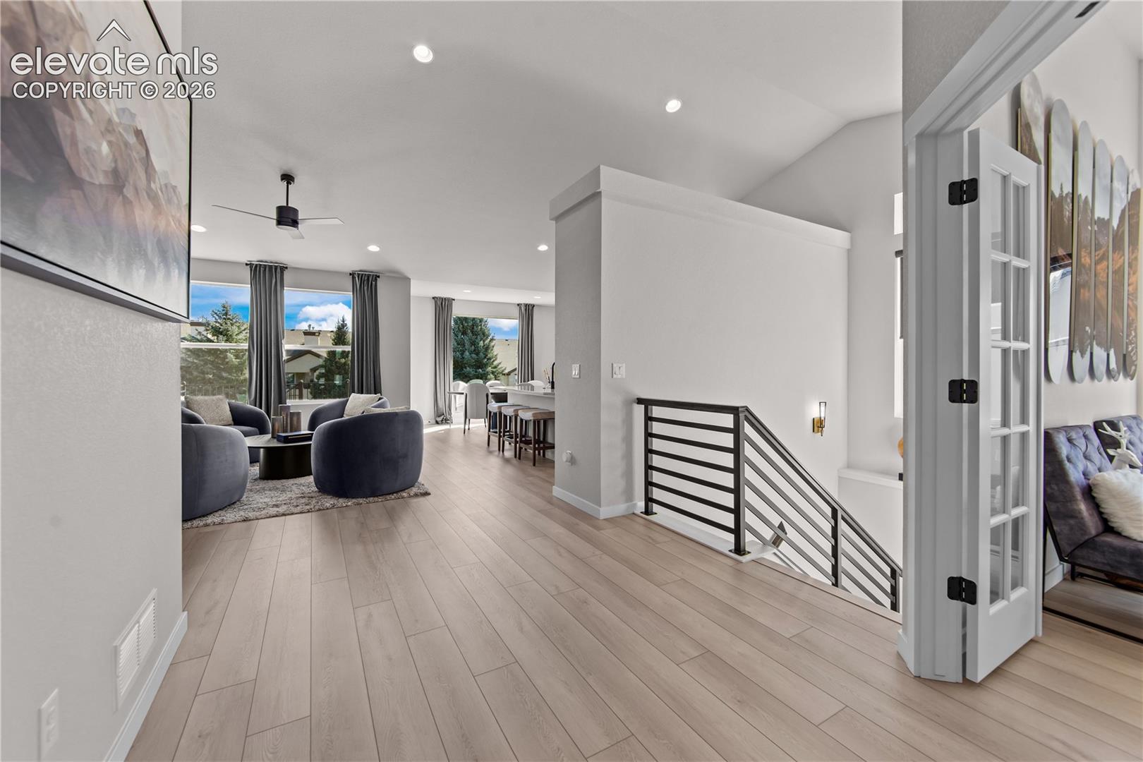Open-concept interior featuring light wood-finish flooring, recessed lighting, and a staircase with a horizontal metal railing