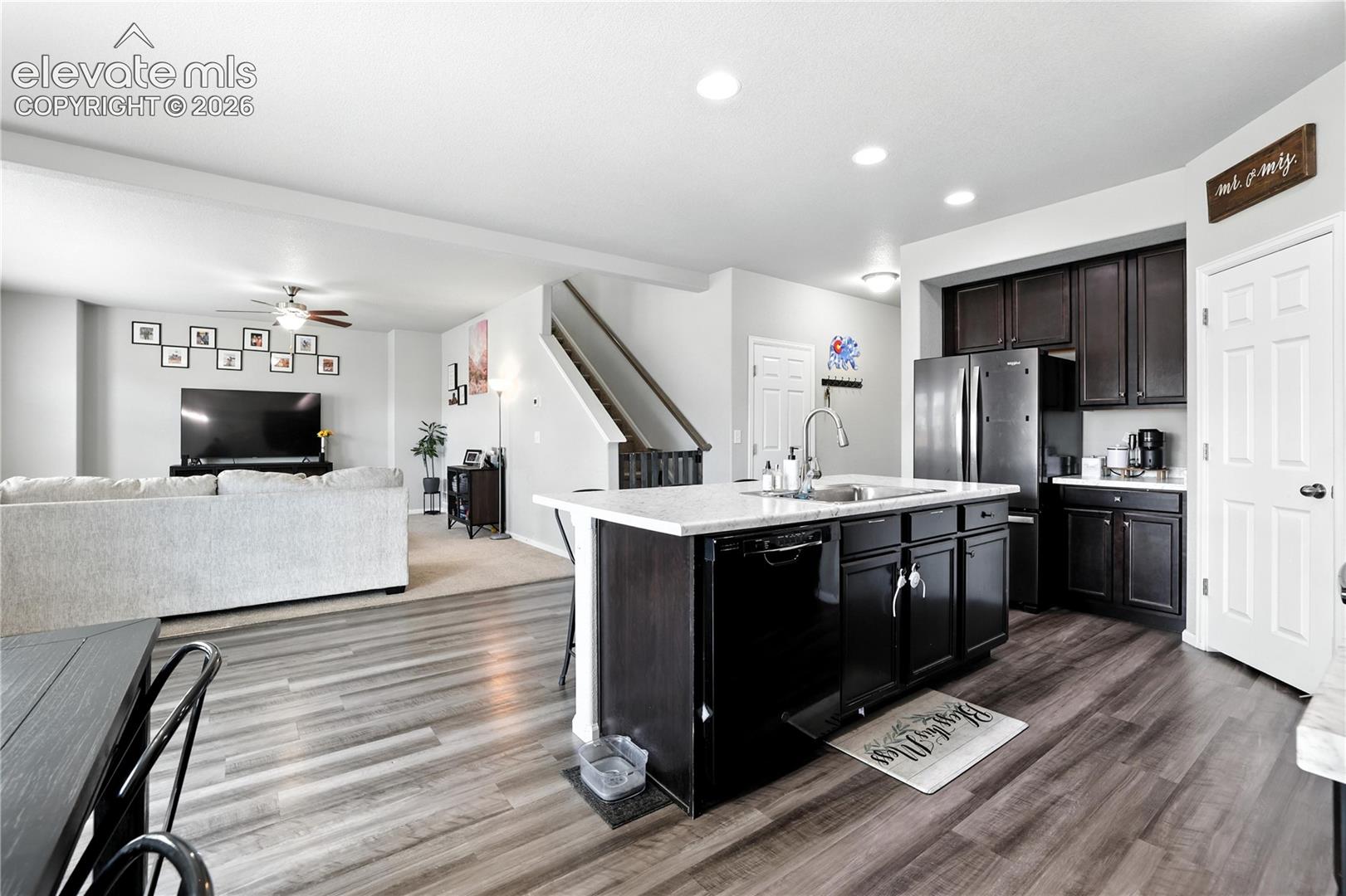 Open-concept layout featuring wood-finish flooring, recessed lighting, dark cabinetry, and an island with a sink and white countertop