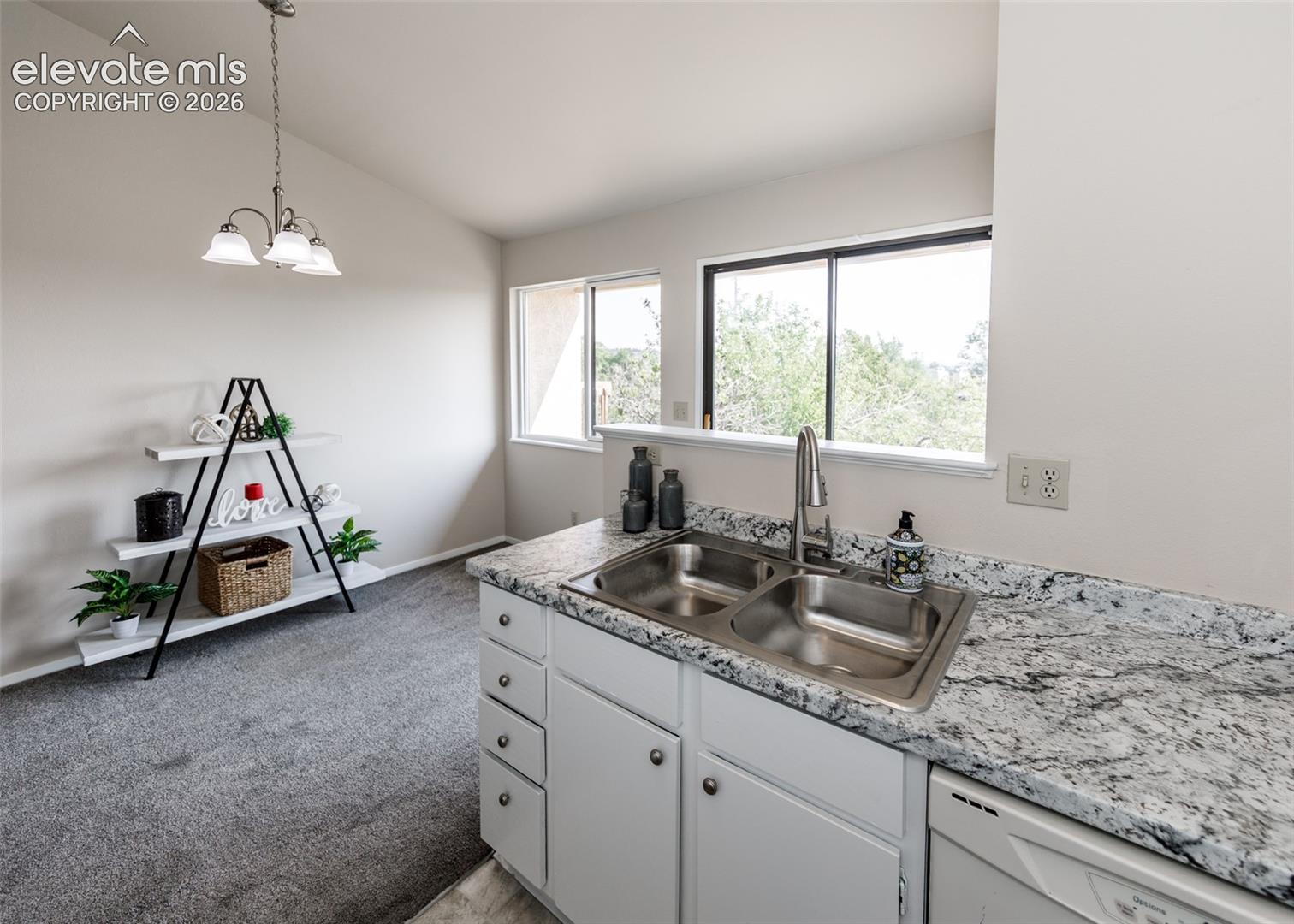 Kitchen area featuring a double basin stainless steel sink, granite-patterned countertop, white cabinetry, and an integrated dishwasher