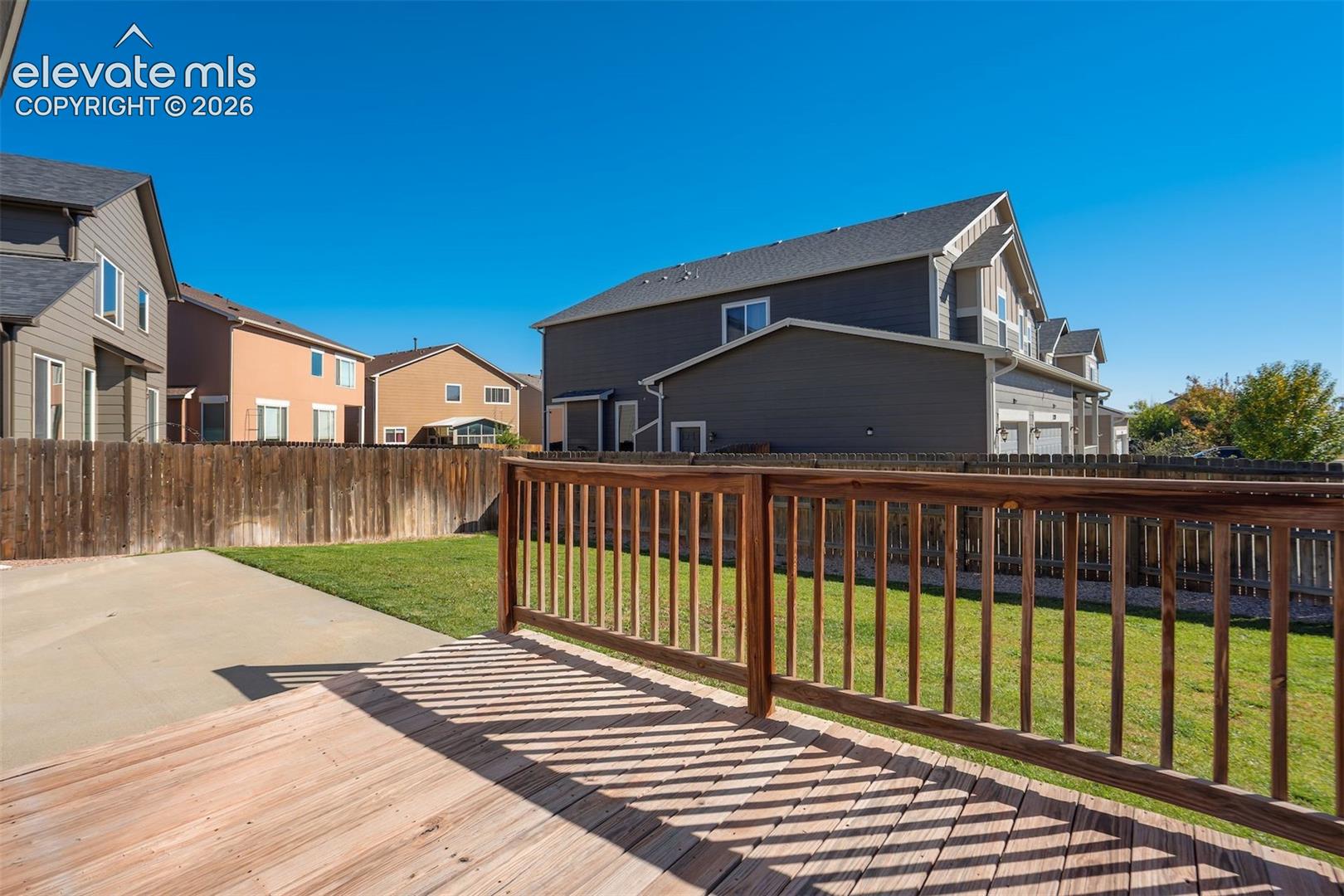 Wood-finish deck with a matching wood railing, concrete patio, and a grass lawn