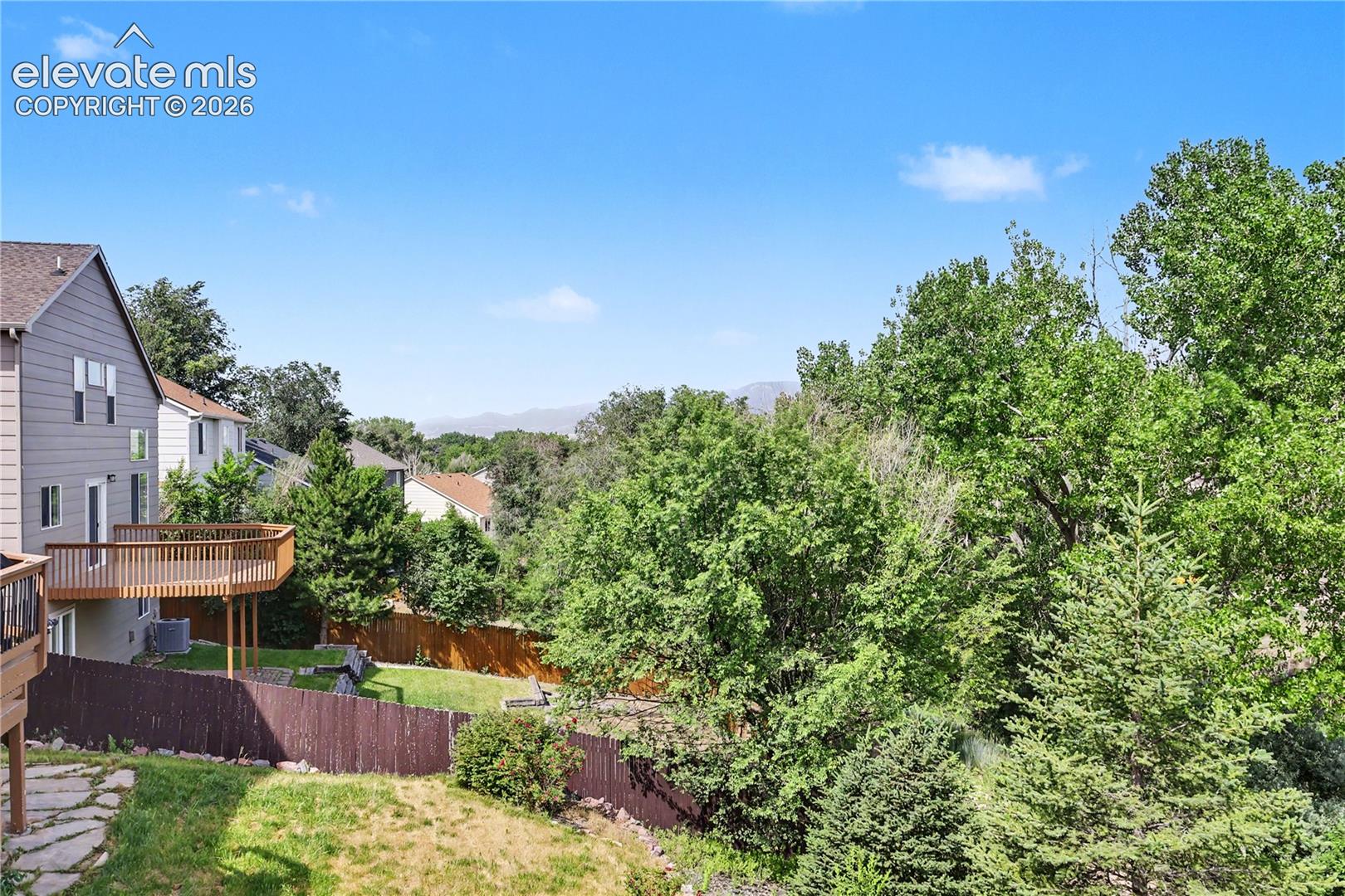 Expansive backyard featuring a multi-level wood deck, privacy fencing, and mature trees. Views of the mountains in person! 