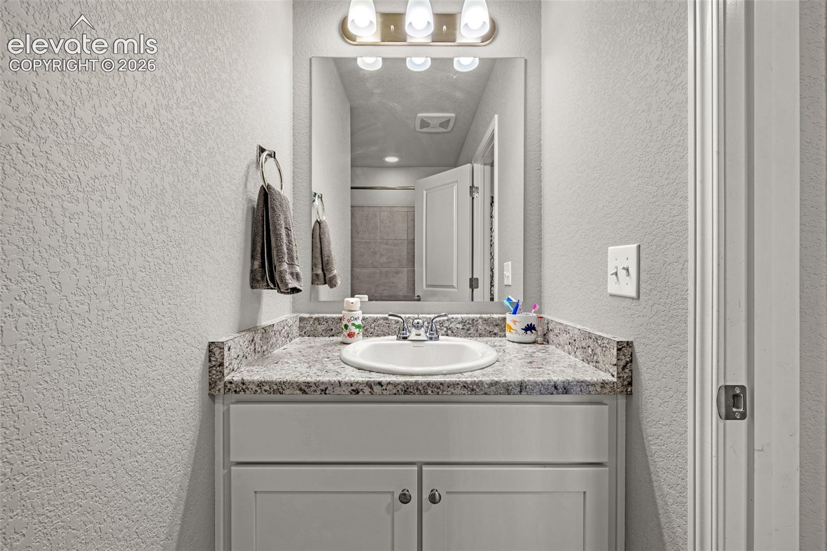 Bathroom vanity featuring a granite-style countertop, undermount sink, and brushed nickel faucet