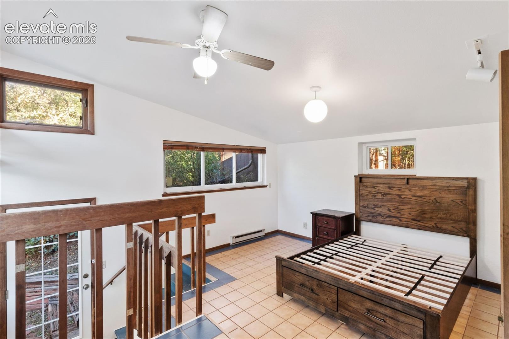 Vaulted ceiling featuring a central lighted ceiling fan, ceramic tile flooring, horizontal windows, and wood-railing staircase enclosure