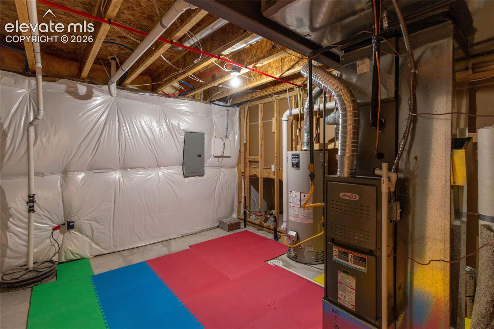 Unfinished utility space featuring a water heater, furnace system, electrical panel, and polyethylene vapor barrier wall insulation