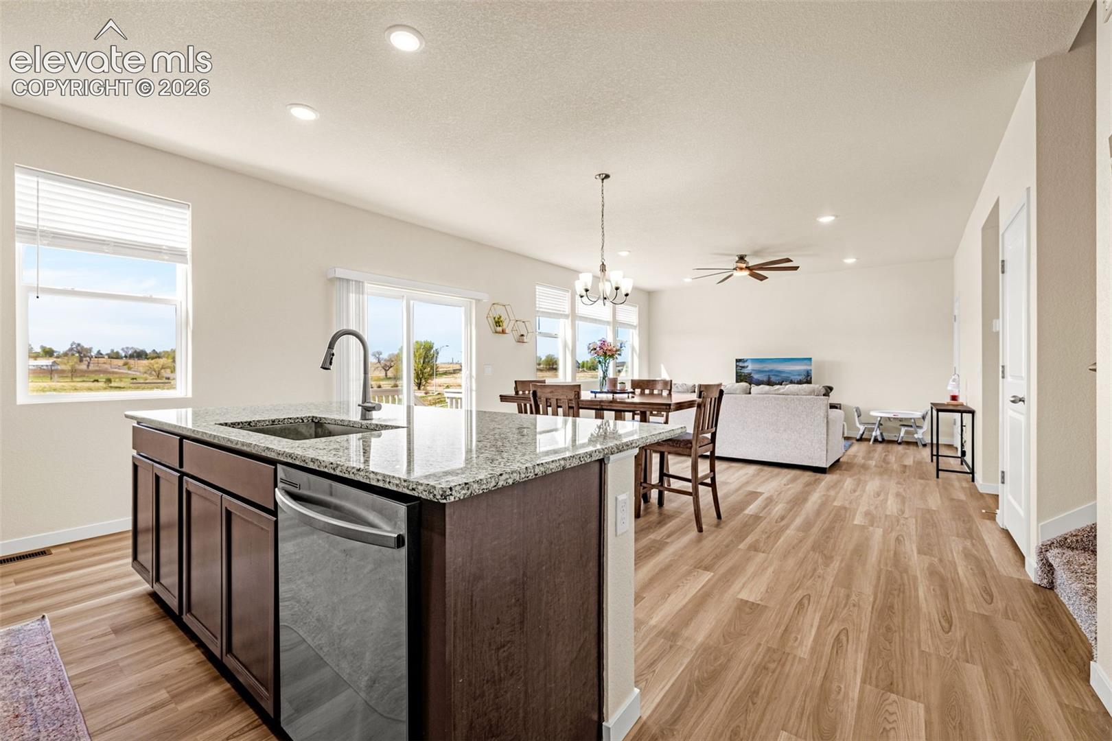 Kitchen island with integrated sink and dishwasher, granite countertop, wood-finish flooring, recessed lighting, and sliding glass door access