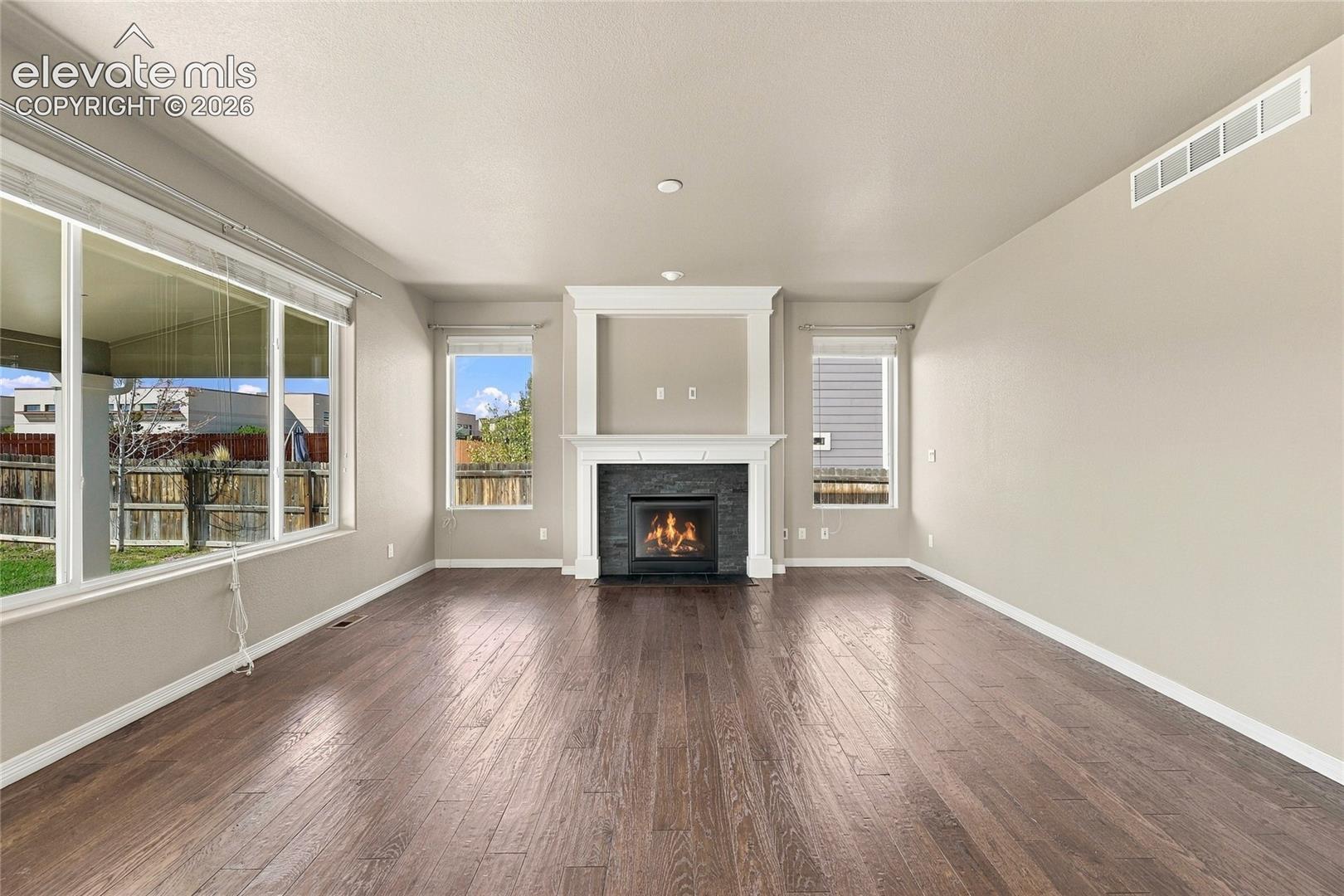 Living area featuring wood-finish flooring, fireplace with a stone-surround facade, custom white mantel, and large picture windows