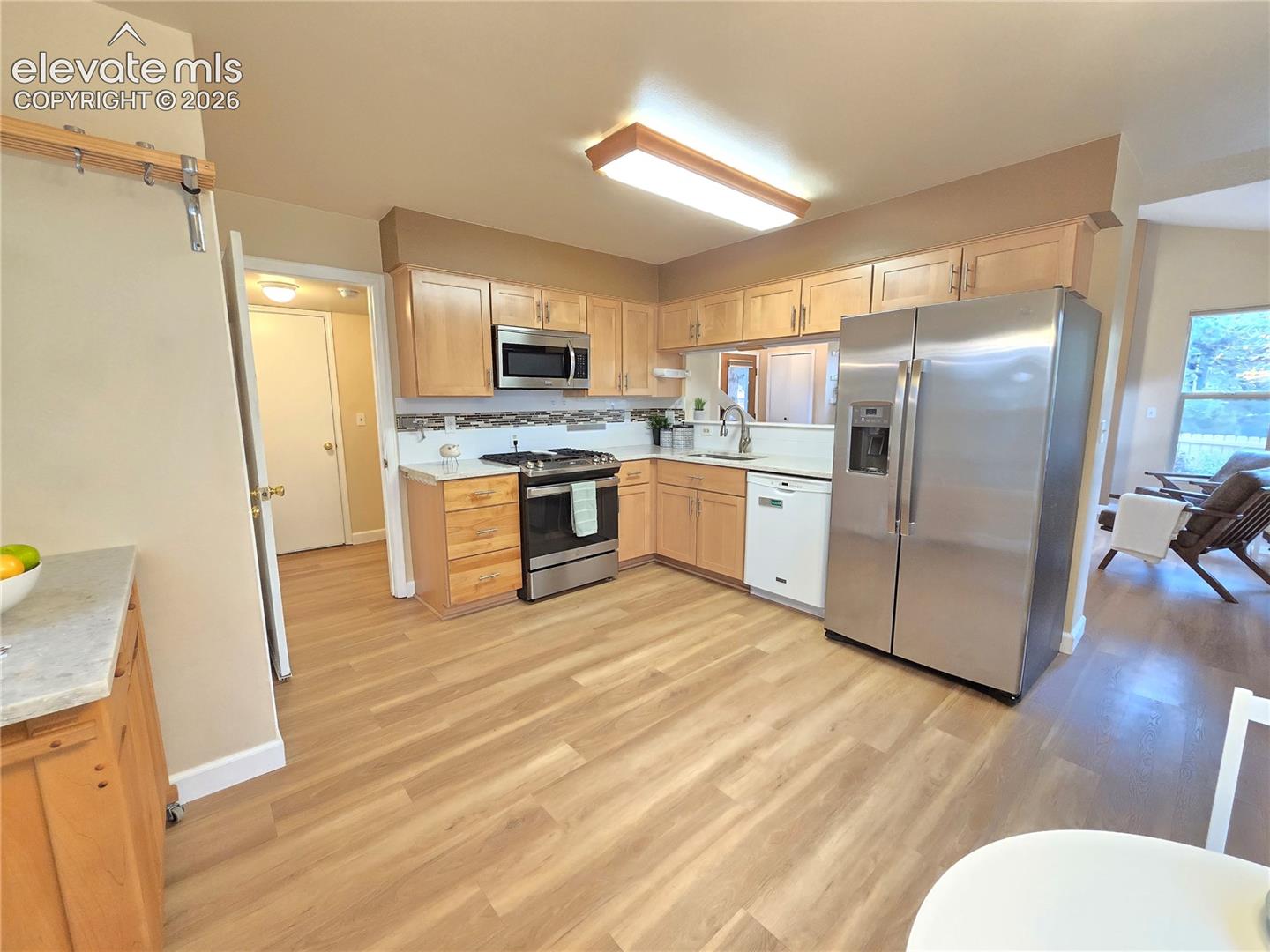 Kitchen featuring light-finish cabinetry, wood-finish flooring, stainless steel appliances, a tile backsplash, and built-in task lighting
