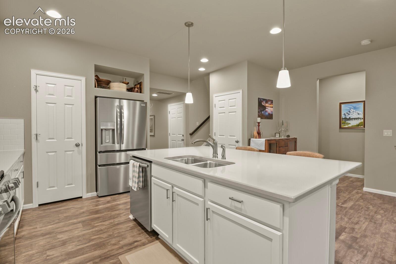 Kitchen featuring a central island with quartz countertops, stainless steel appliances, white cabinetry, recessed lighting, and wood-finish luxury tile flooring
