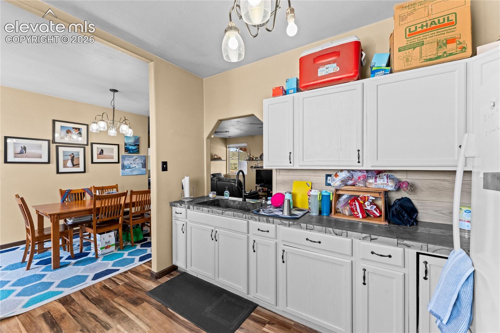 Kitchen area featuring white shaker-style cabinetry, dark stone-finish countertops, an undermount sink with a gooseneck faucet, and wood-finish flooring