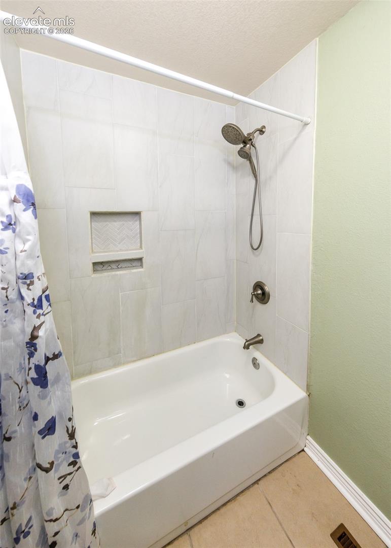 Bathtub with wall-mounted shower fixture, tiled surround with recessed niche, and light-colored flooring