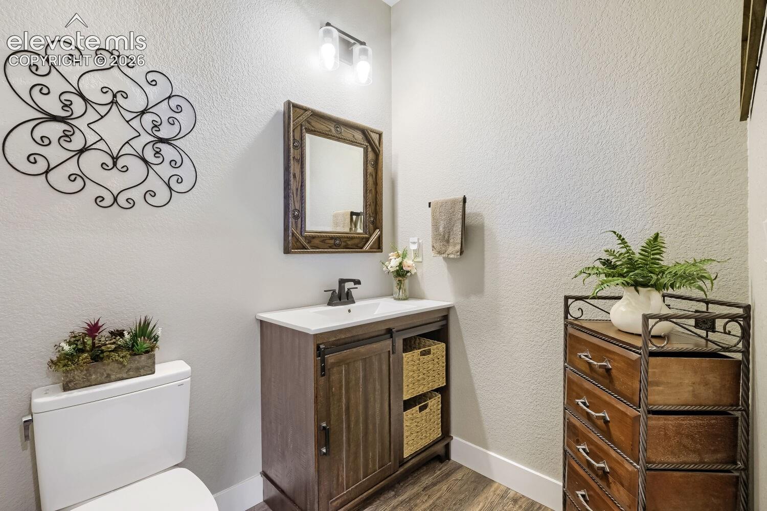 Wood-finish flooring with a white vanity featuring a ceramic sink, dark bronze faucet, and an ornate framed mirror
