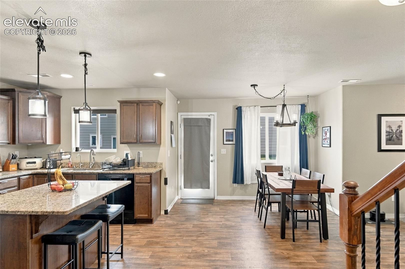 Open-concept kitchen and dining area featuring stone-surface countertops, wood-finish cabinetry, wood-finish flooring, recessed lighting, and decorative pendant fixtures