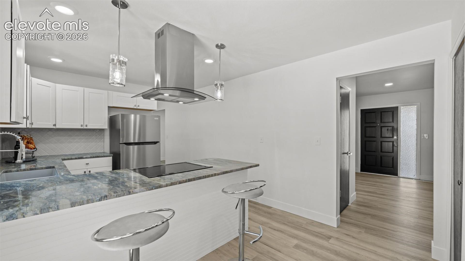 Kitchen featuring white cabinetry, stainless steel appliances, a range hood, and pendant lighting