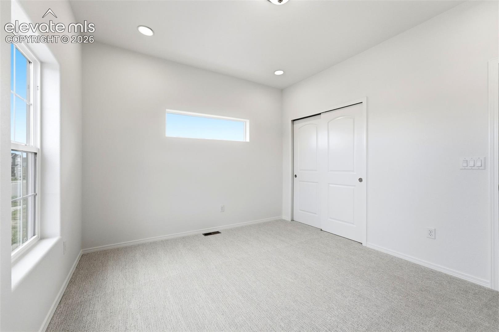 Room featuring neutral carpeting, recessed ceiling lighting, a horizontal transom window, a tall rectangular window, and dual-panel closet doors