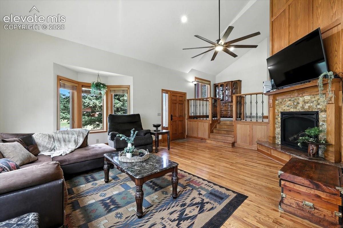Vaulted ceilings, wood-finish flooring, floor-to-ceiling fireplace with stacked-stone surround, wooden paneling, and bay windows