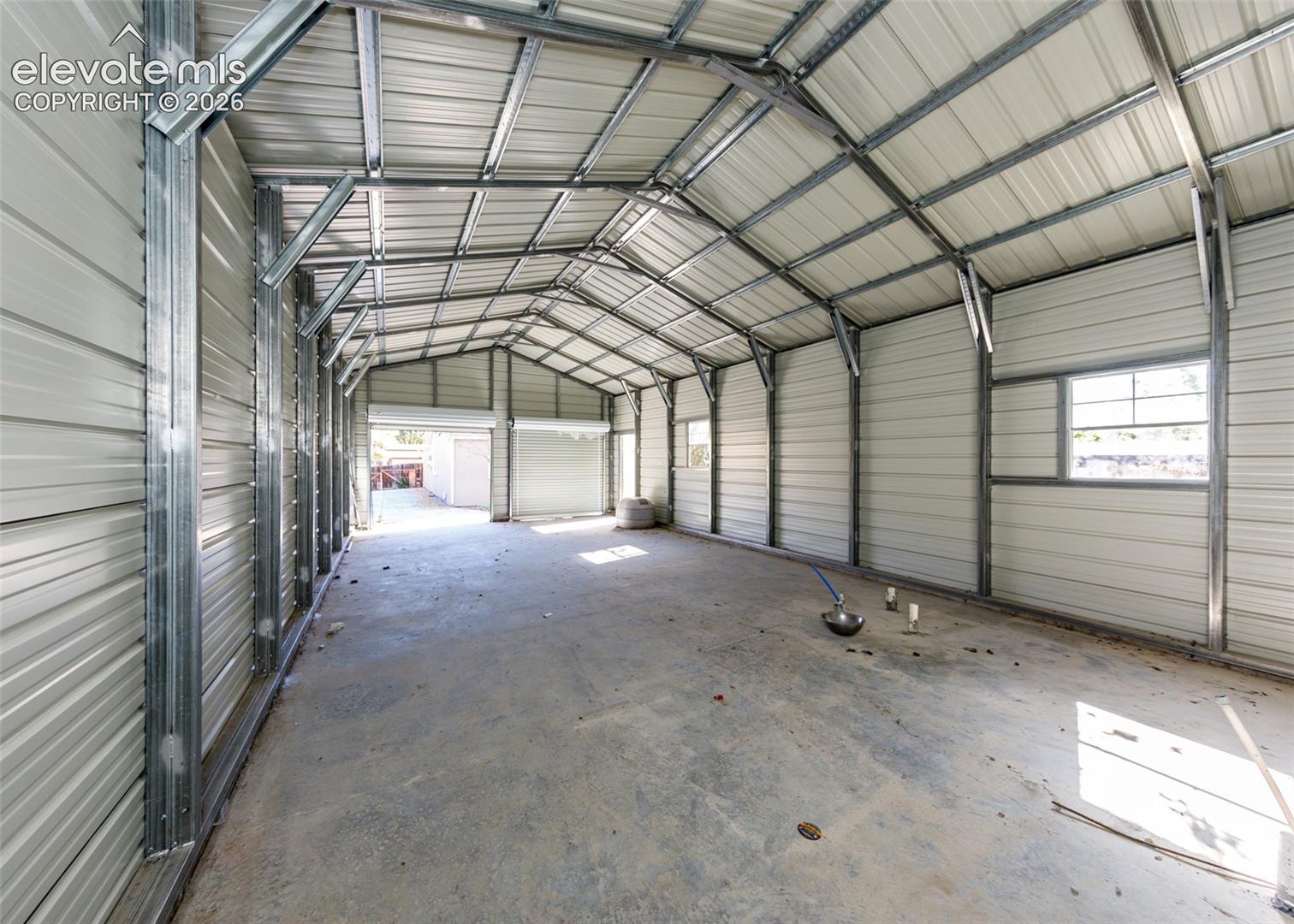 Expansive metal outbuilding featuring a galvanized steel frame, corrugated metal walls and roof, concrete flooring, and multiple windows
