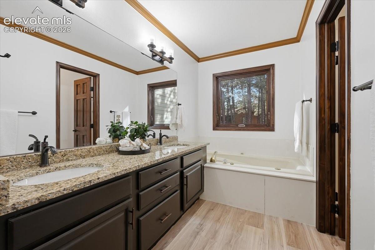 Dual vanity with granite countertop and undermount sinks, bronze fixtures, wood-finish flooring, and a built-in soaking tub